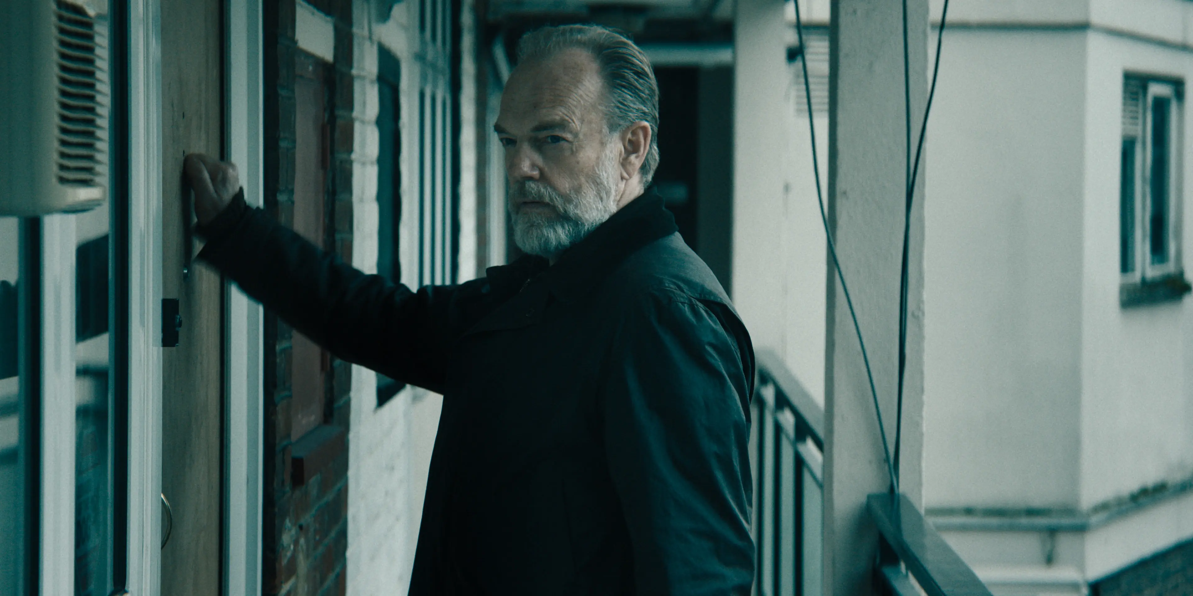 Frank Harkness raises a hand to a door and looks back over his shoulder.