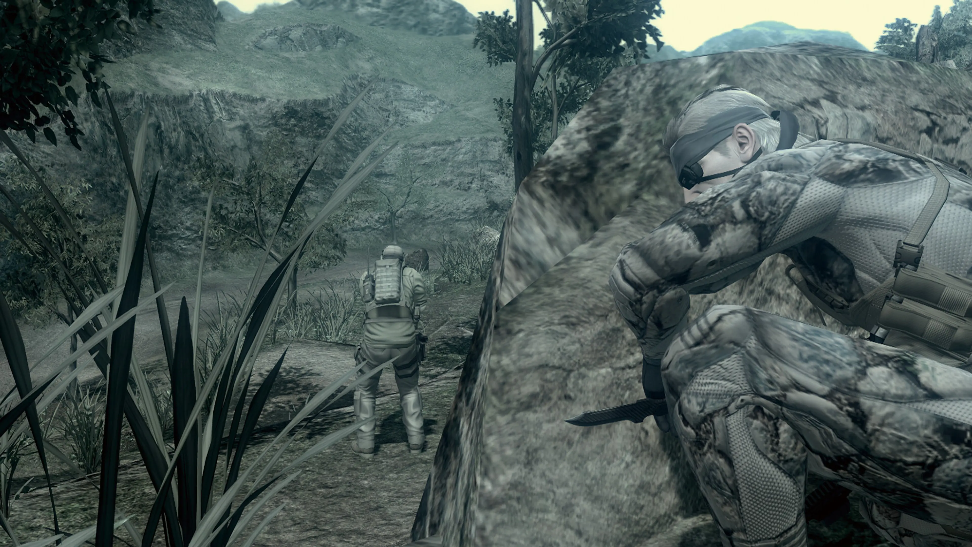 Solid Snake crouches behind a rock while another soldier walks through a jungle in METAL GEAR SOLID: MASTER COLLECTION Vol. 2.