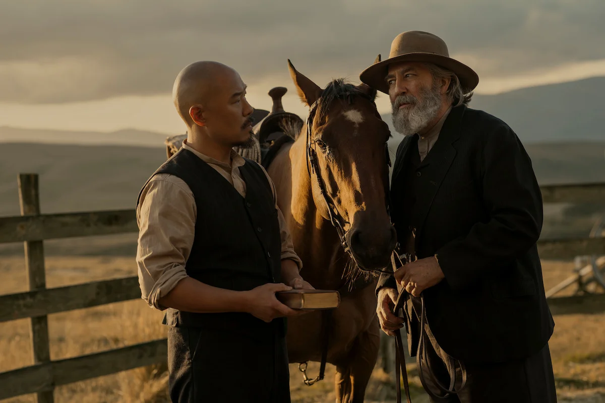Lee holds a book while Samuel Hamilton stands beside a horse at sunset.