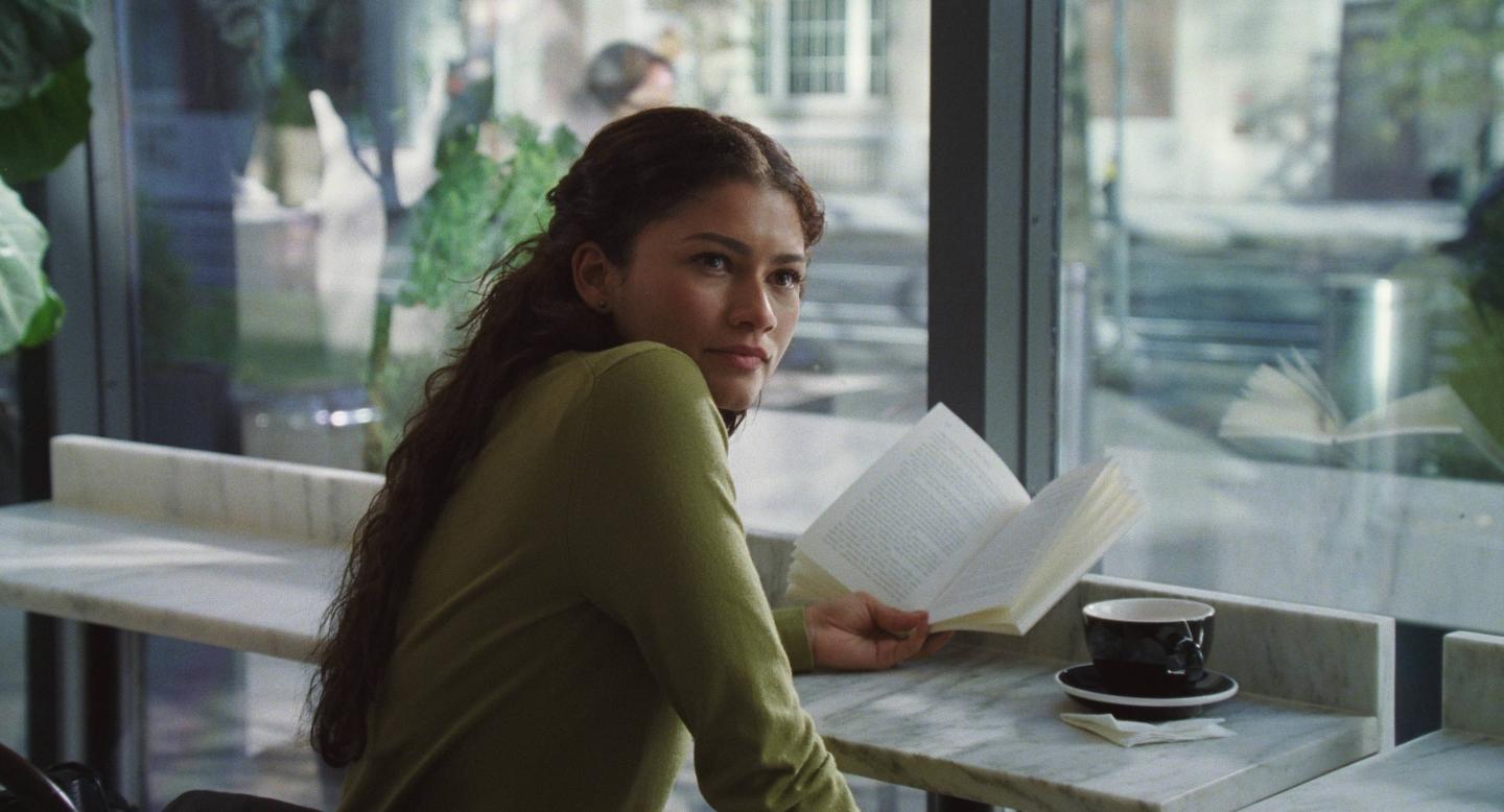 Emma looks up from an open book beside a café window.