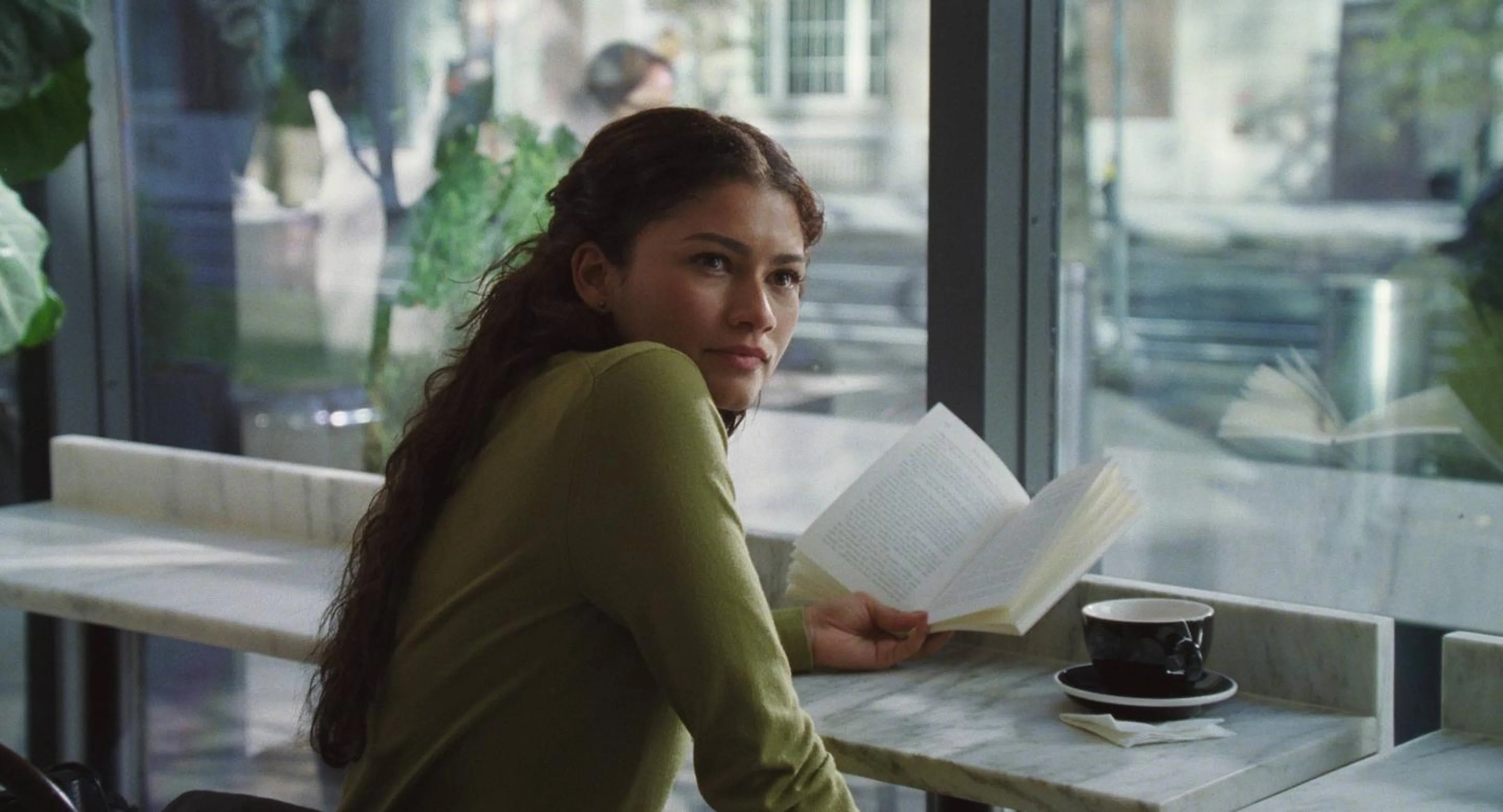 Emma looks up from an open book beside a café window.