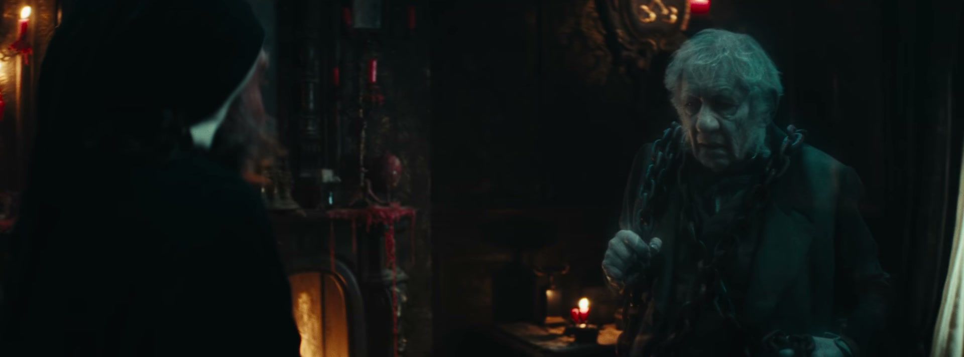 Ian McKellen’s chained ghost faces Scrooge in a candlelit room.