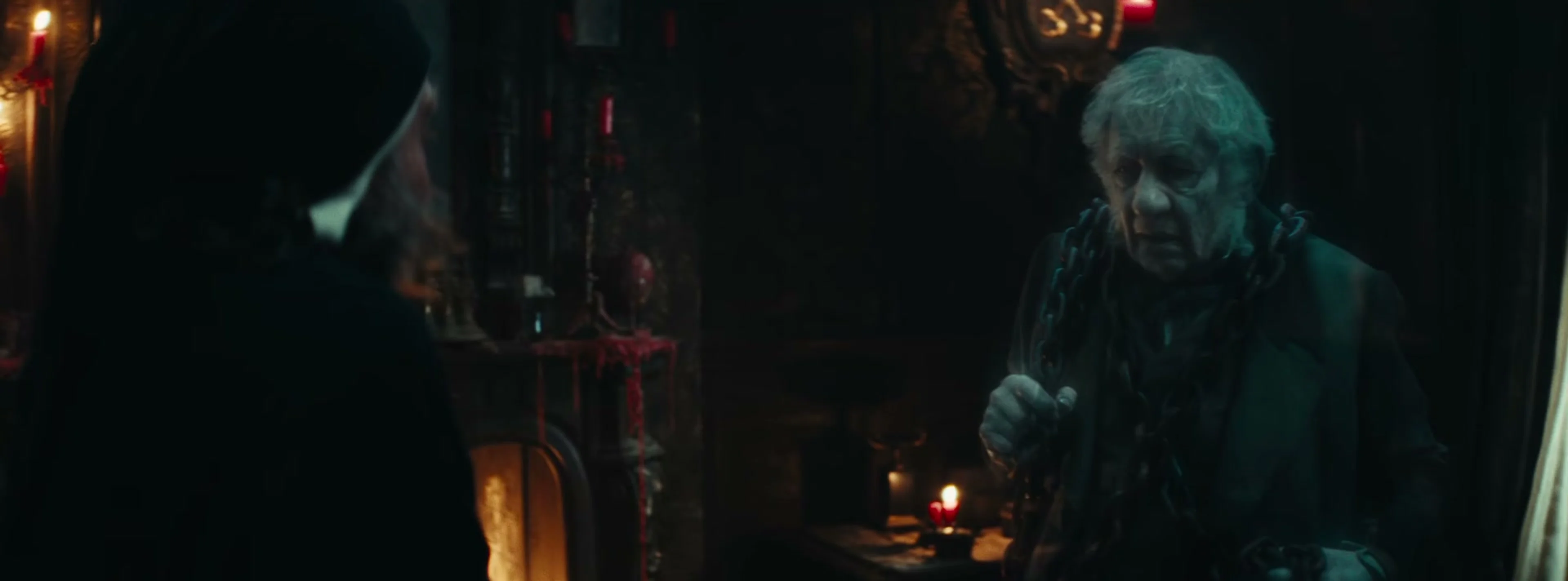 Ian McKellen’s chained ghost faces Scrooge in a candlelit room.