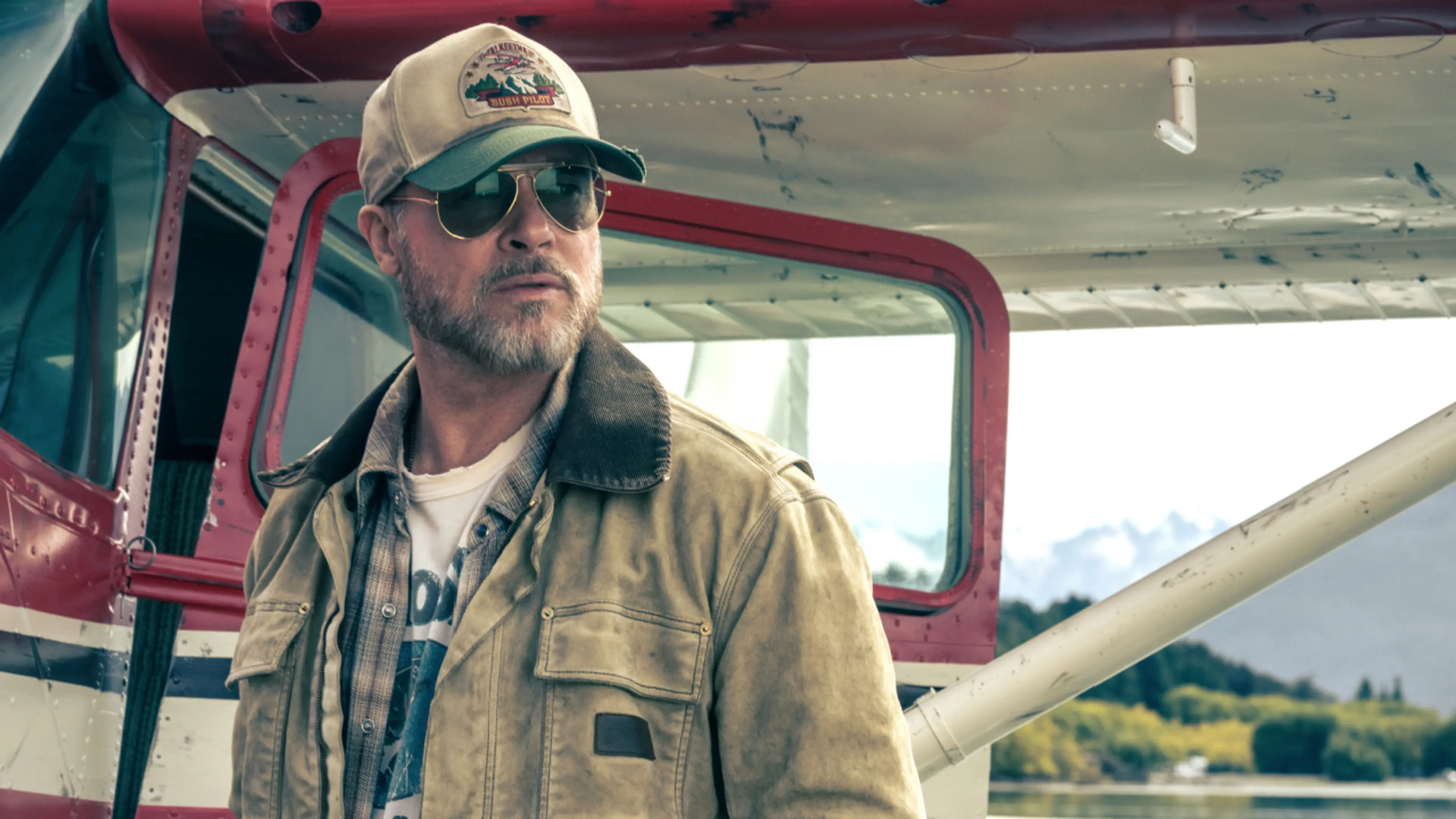 Brad Pitt as James Belmont stands beside a red and white plane.