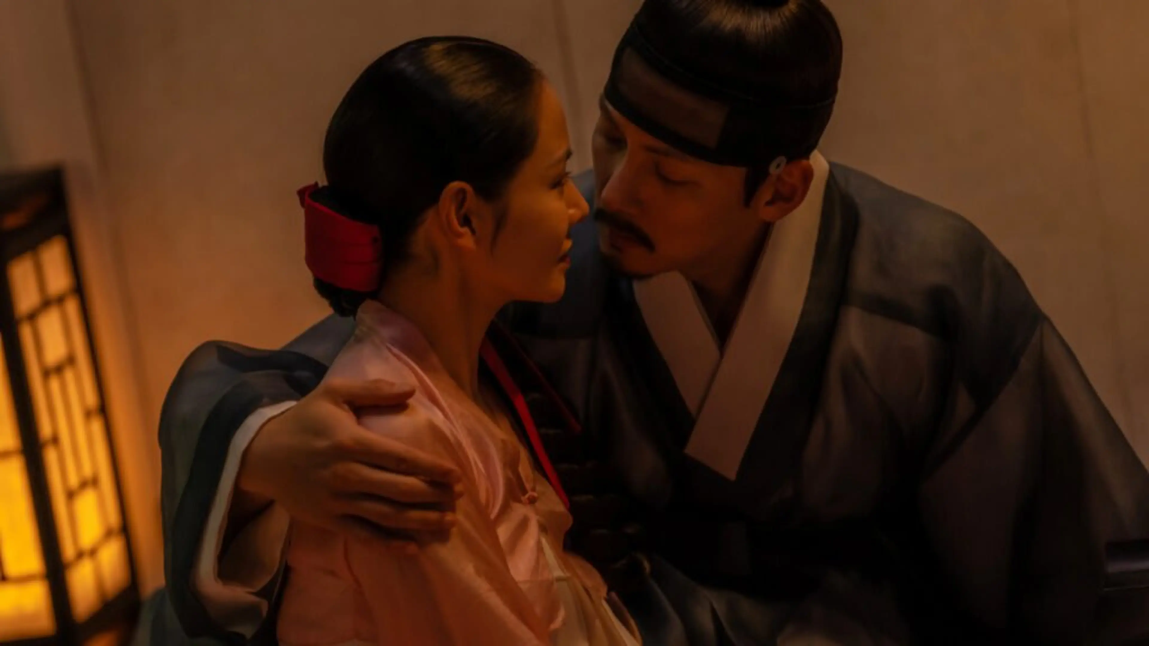 Lady Cho and Cho Won sit close together in a room lit by a lantern.