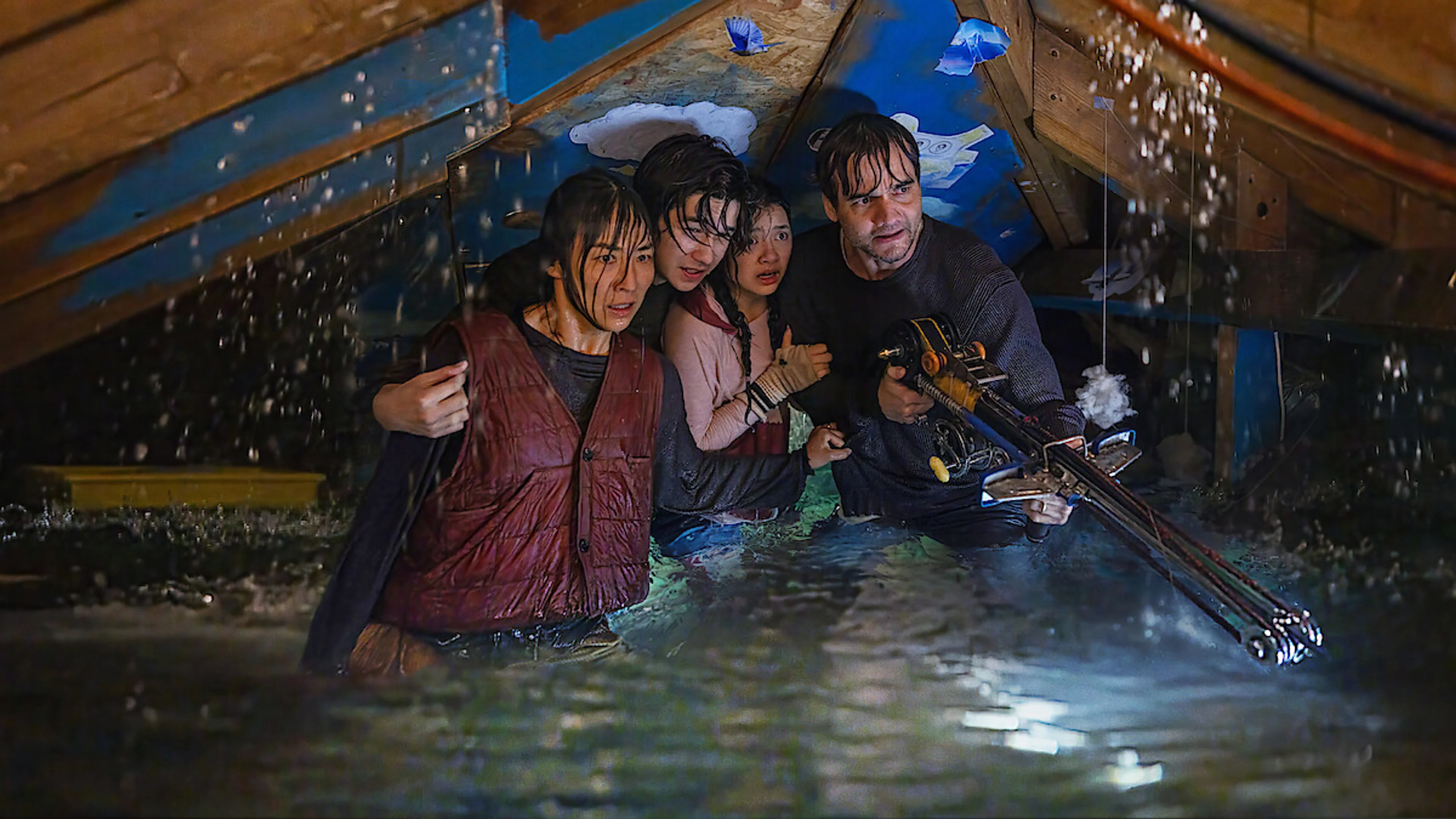 The Last House family huddles in a flooded attic while one man holds a crossbow.