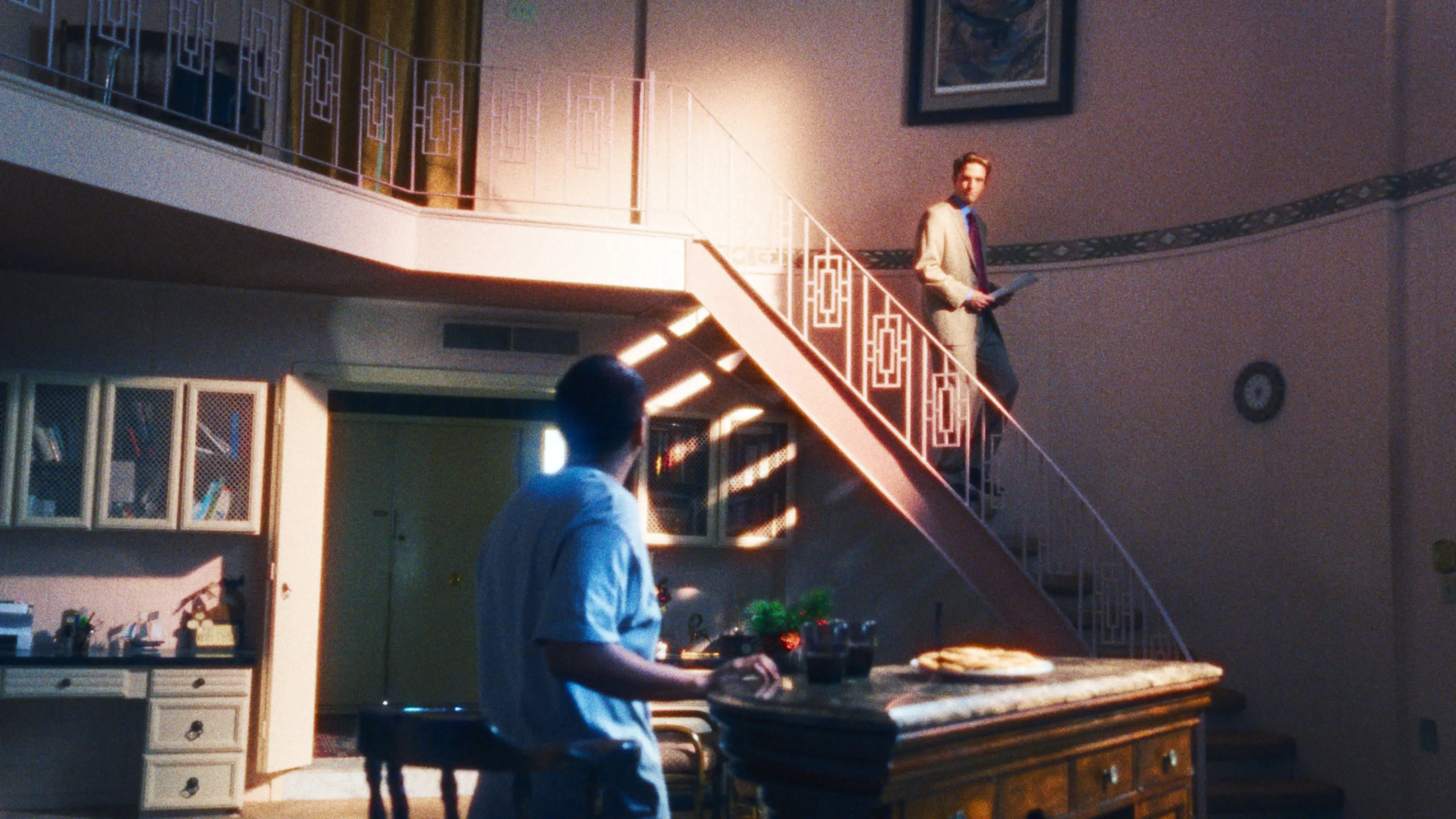 A man stands at the kitchen counter while Hansen looks down from a staircase.