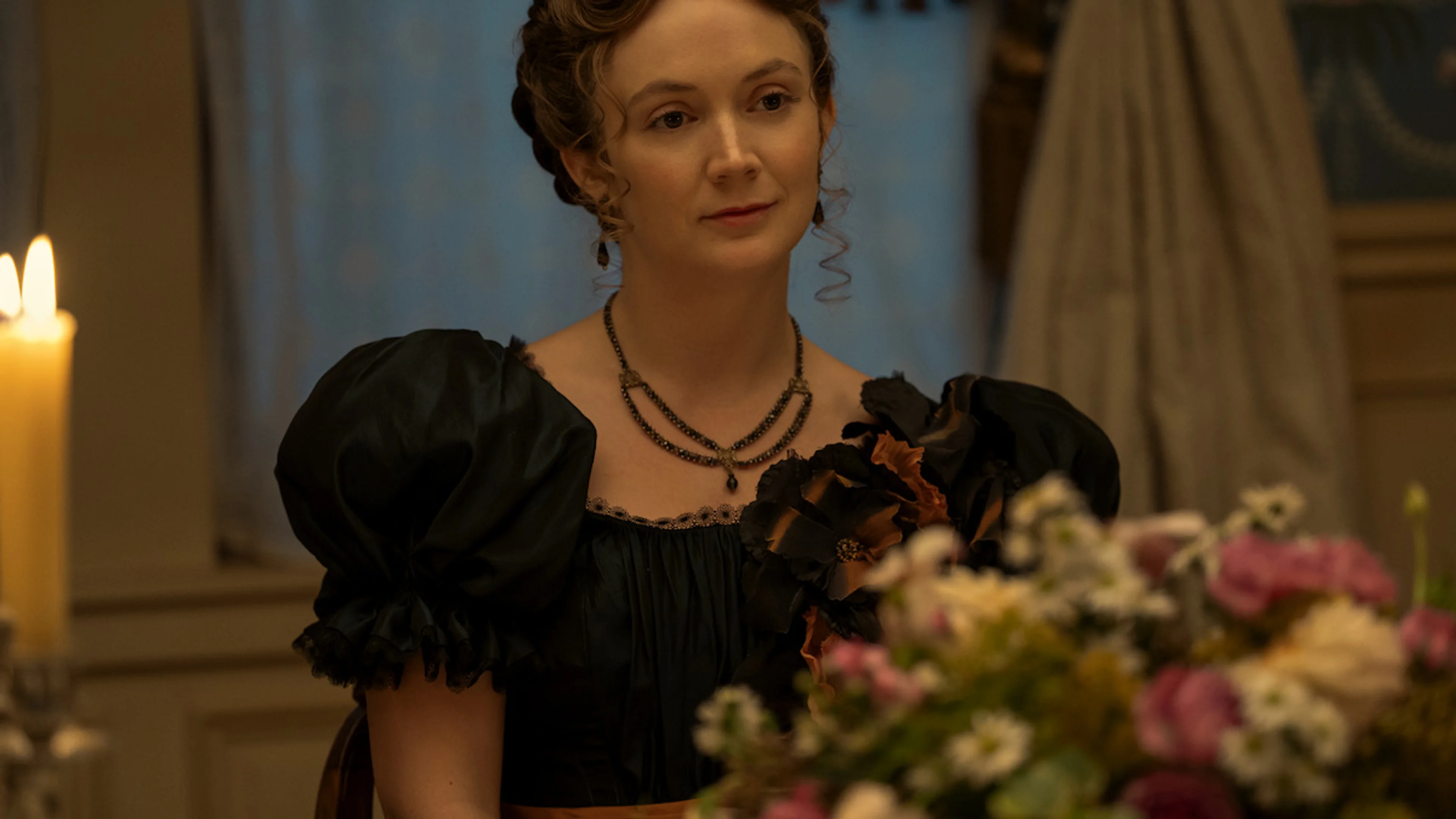 Jessica Barden as Nance O’Neil sits at a flower-covered dinner table in Monster: The Lizzie Borden Story.