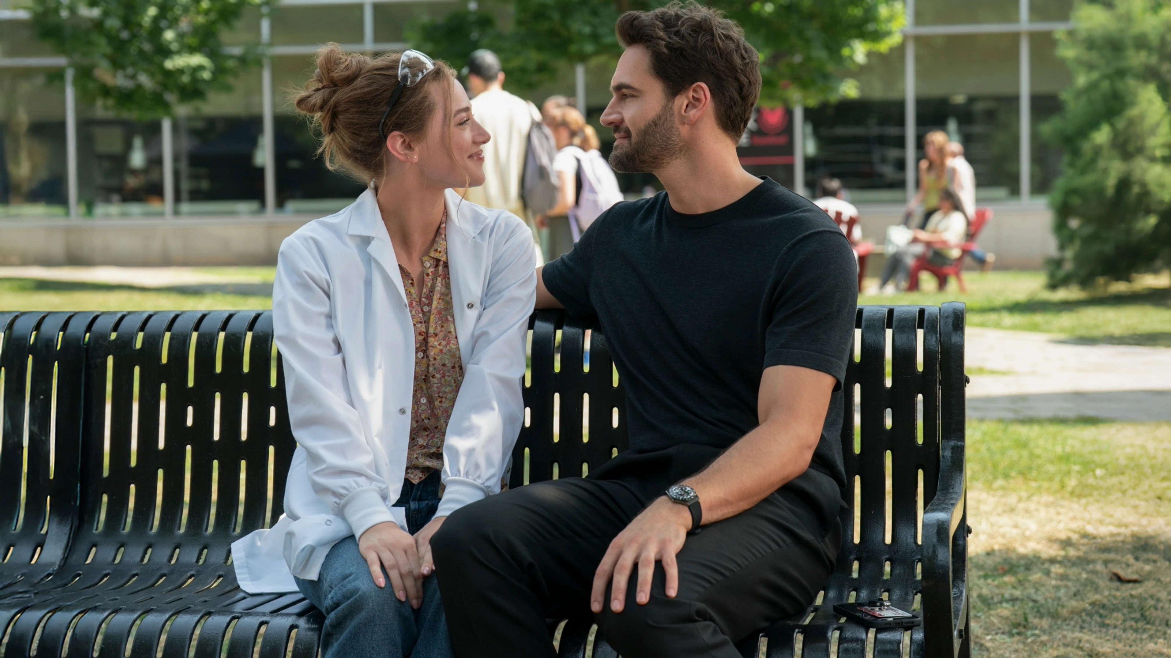 Lili Reinhart and Tom Bateman look at each other on a park bench in The Love Hypothesis.