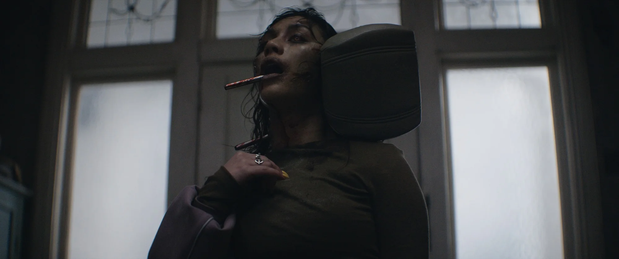 Luciane Buchanan as the possessed Thya, with a car headrest beside her neck.