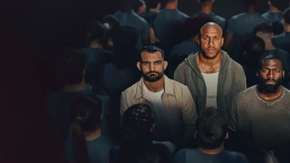 Three coaches stand before a crowd inside the arena for Netflix’s MMA competition The Arena.
