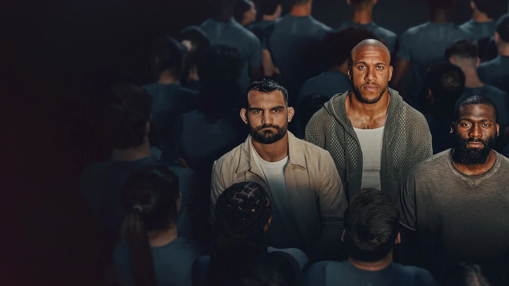 Three coaches stand before a crowd inside the arena for Netflix’s MMA competition The Arena.