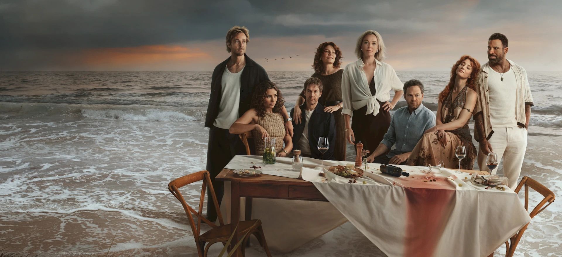 The ensemble cast of The Perfect Lie gathers around a dinner table beside the sea.