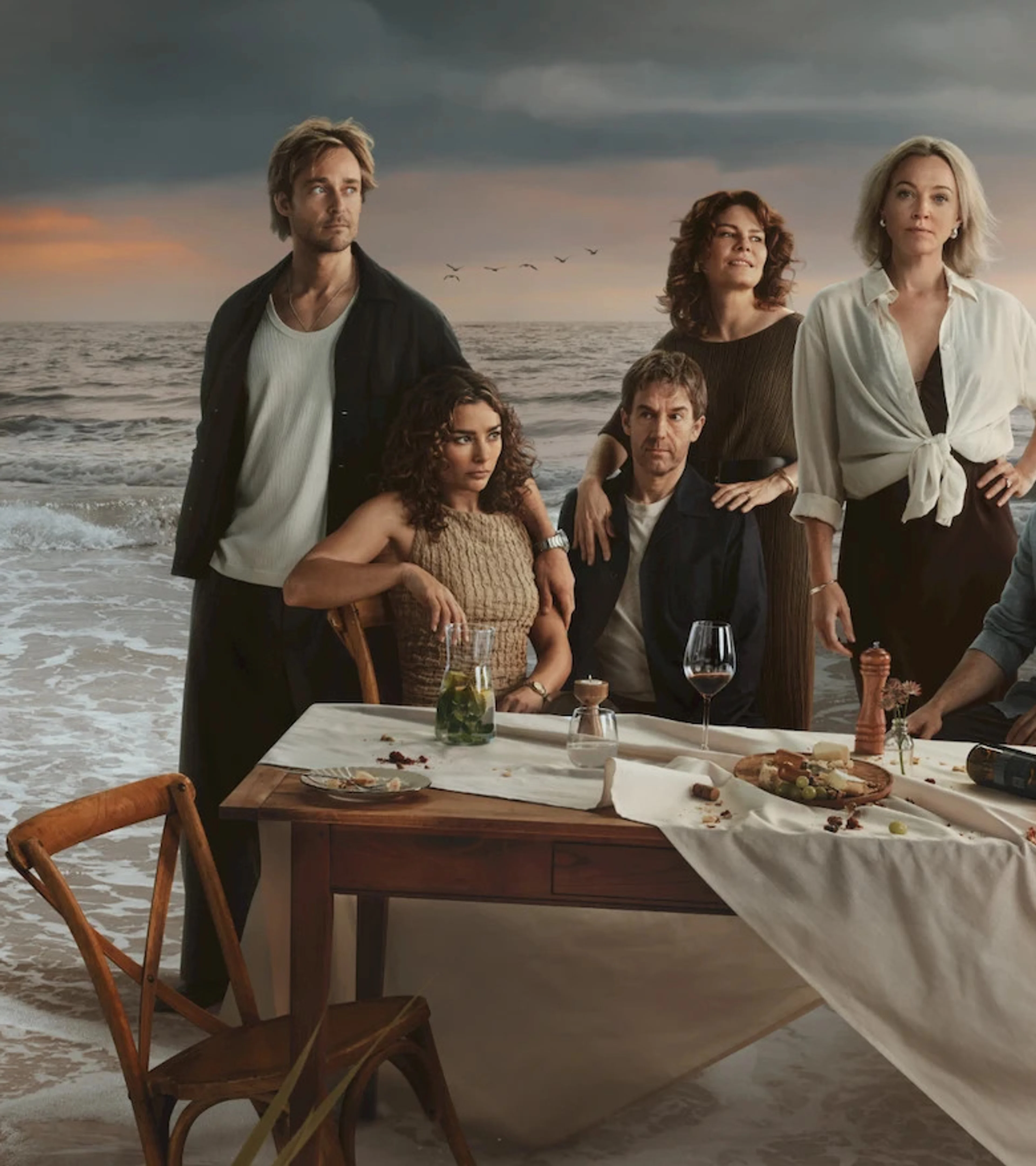 The ensemble cast of The Perfect Lie gathers around a dinner table beside the sea.