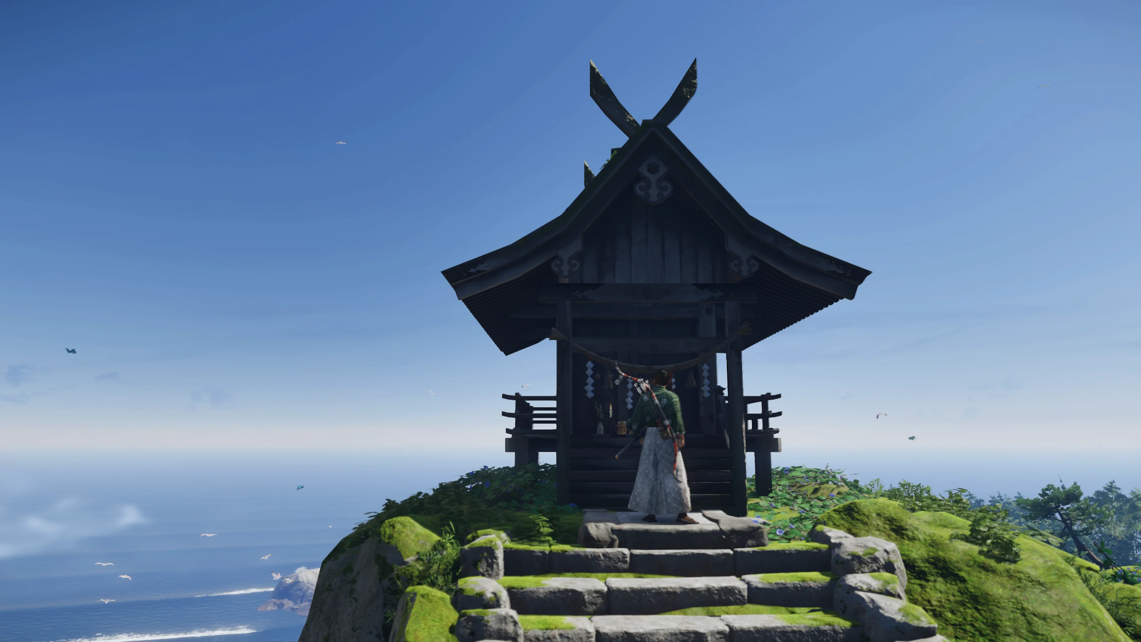 A small wooden shrine stands at the top of a hill with sea and sky beyond it.