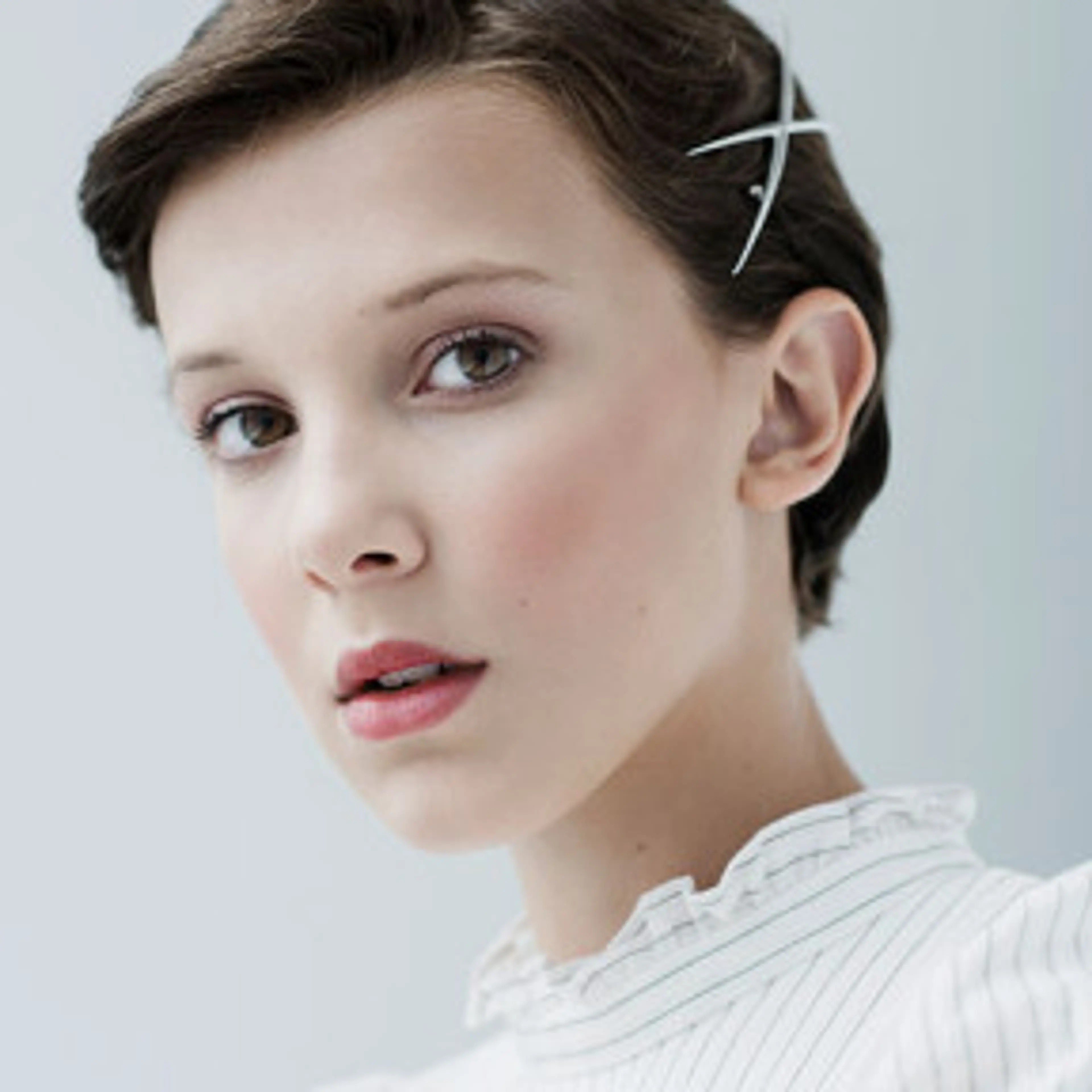 Archive portrait of Millie Bobby Brown with short hair and a white striped blouse.