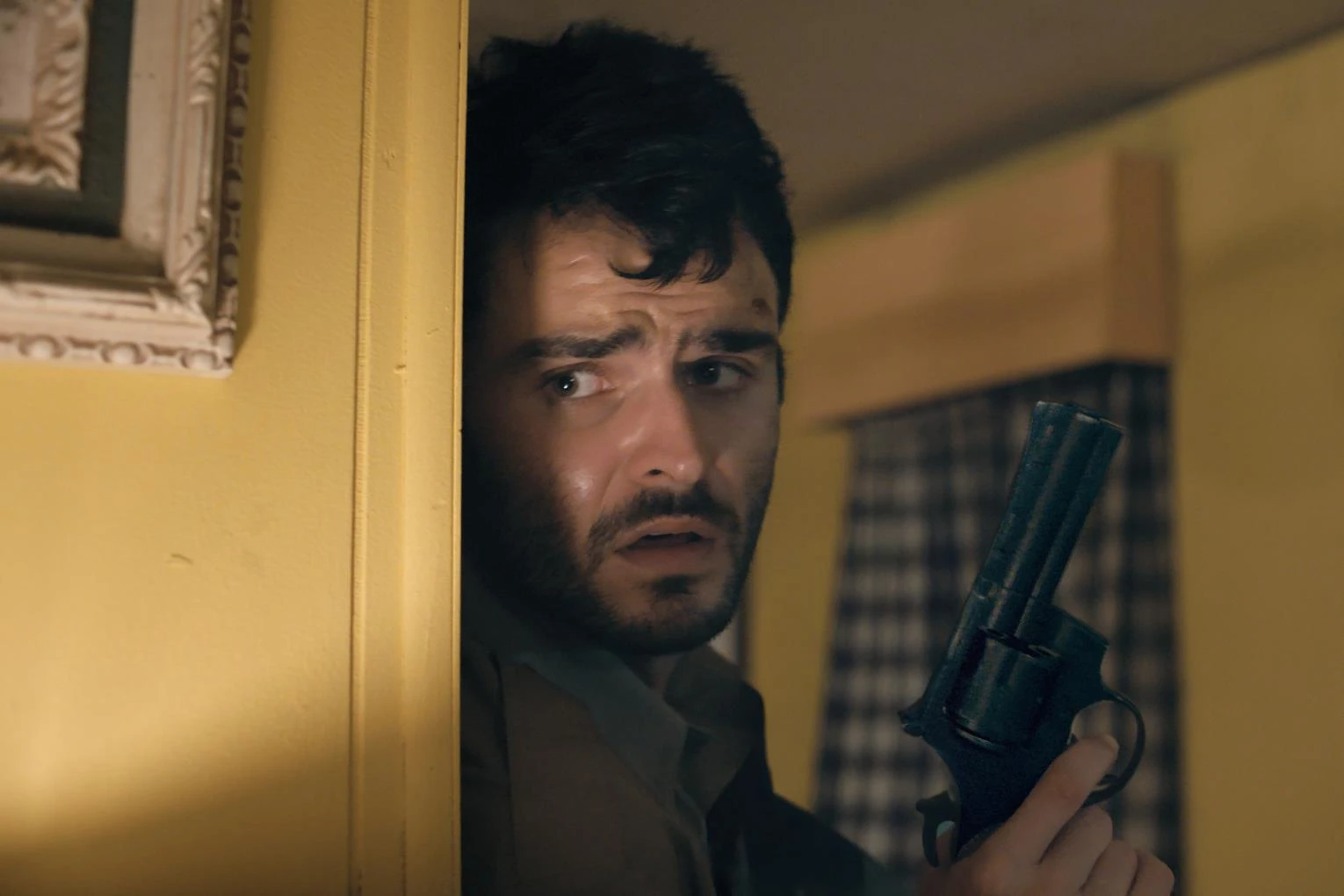 Duke Nicholson peers around a door with a revolver in a scene from The Deputy.