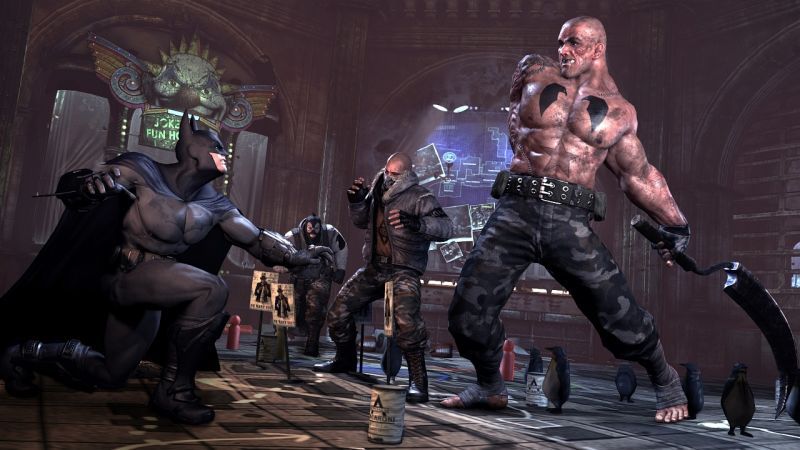 Batman crouches before a large muscular opponent in a colorful Joker-themed room.