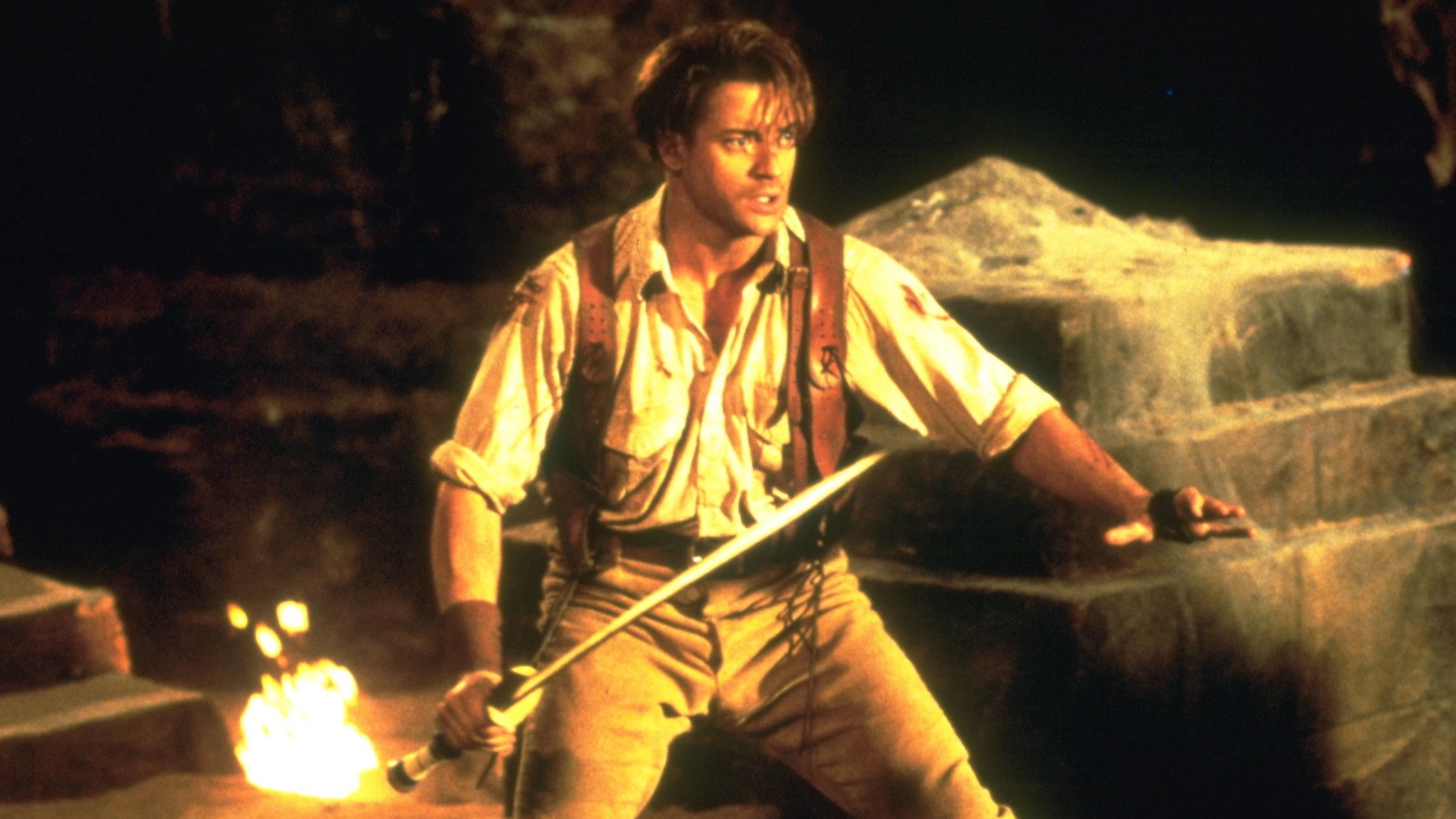Brendan Fraser as Rick O’Connell holds a flaming torch inside an ancient tomb in The Mummy.