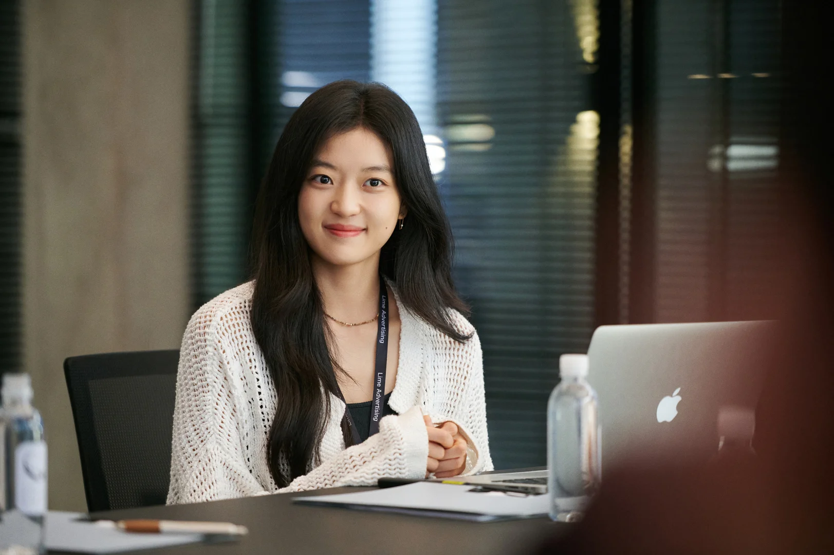 Sun Qian smiles at an open laptop on her desk while wearing a white cardigan and lanyard.