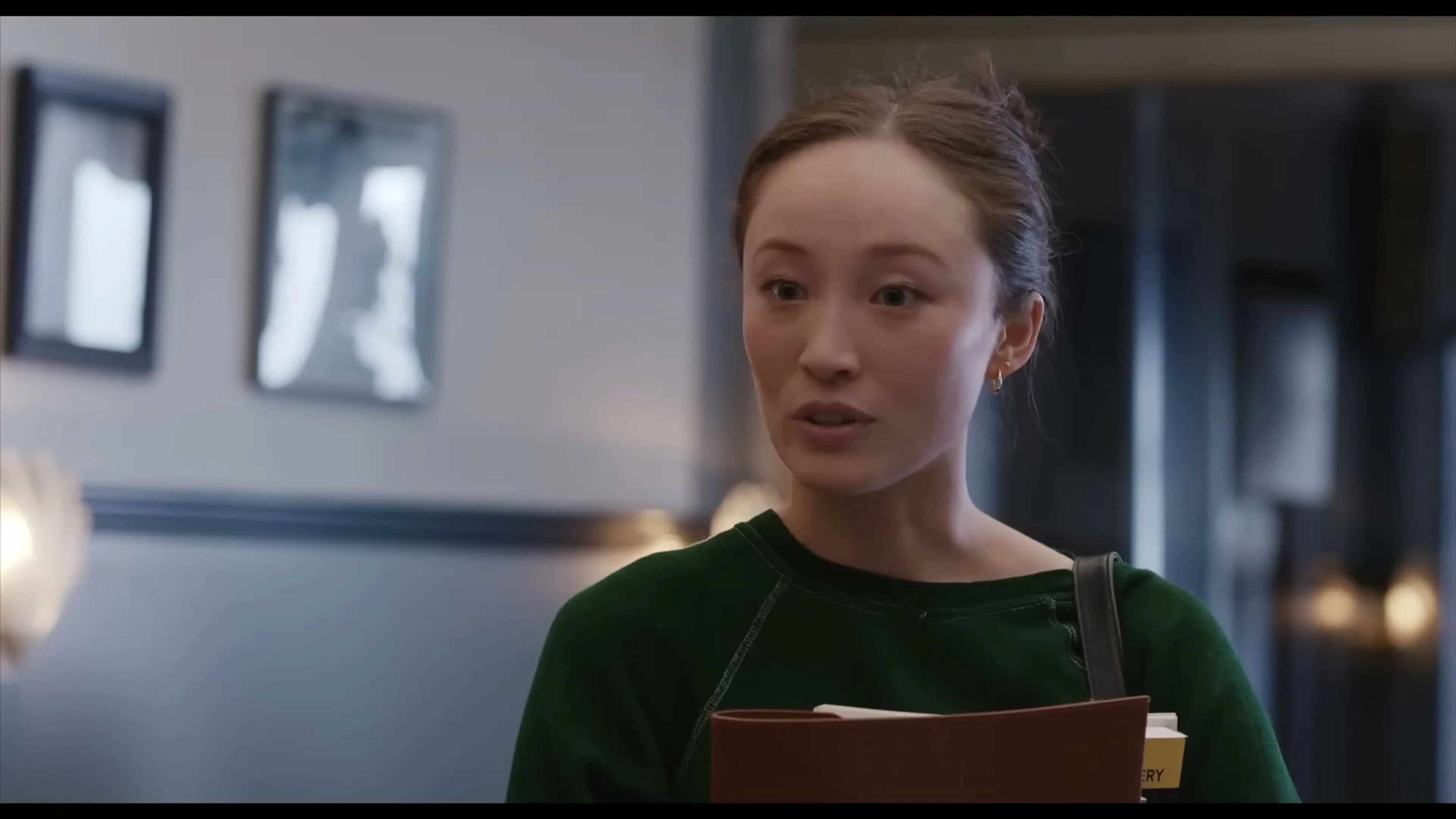Ruthie carries a folder and a paper cup inside a building.