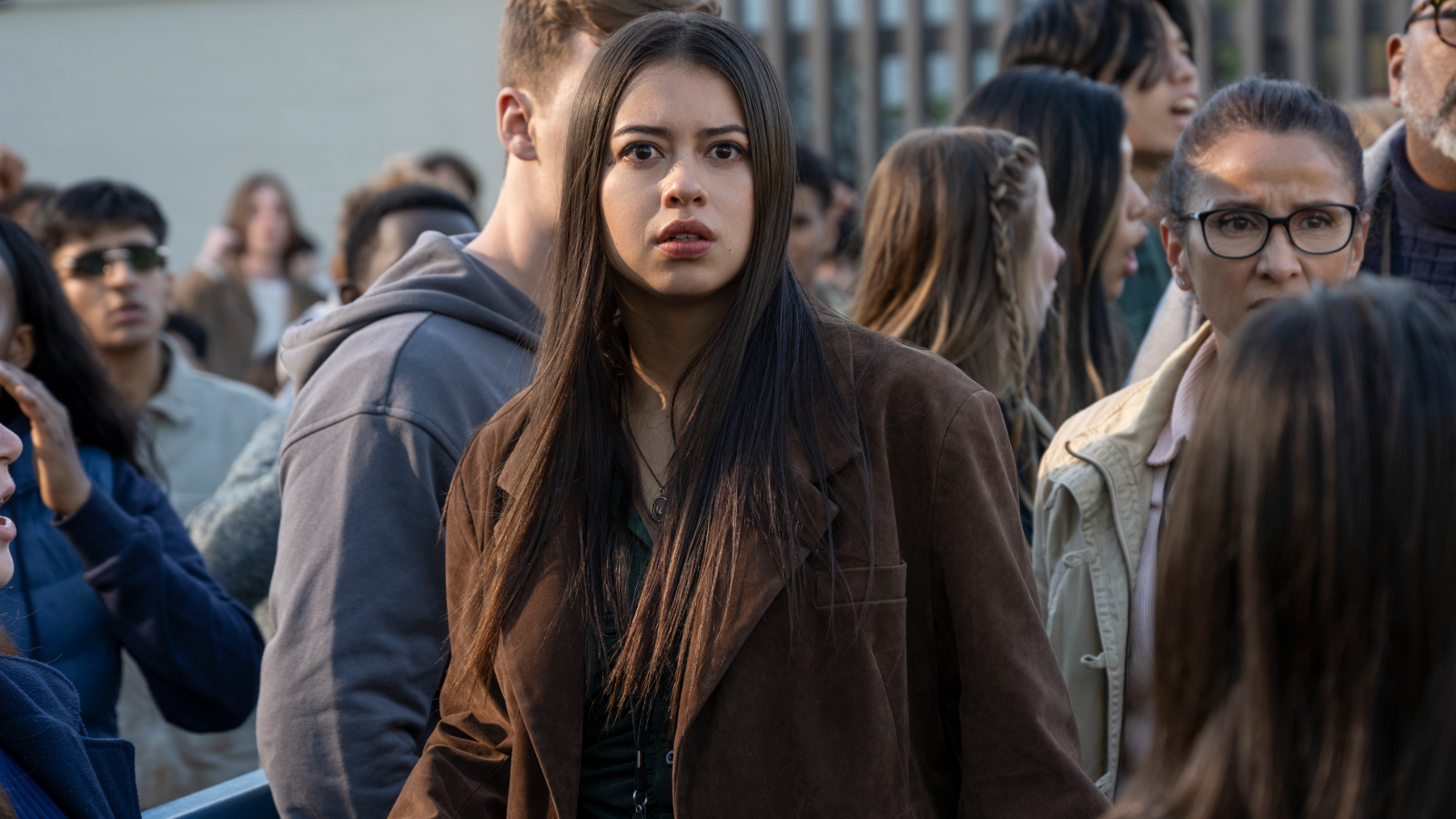 Amber Midthunder as Rita Desjardin stands among a crowd and looks toward someone in front of her.