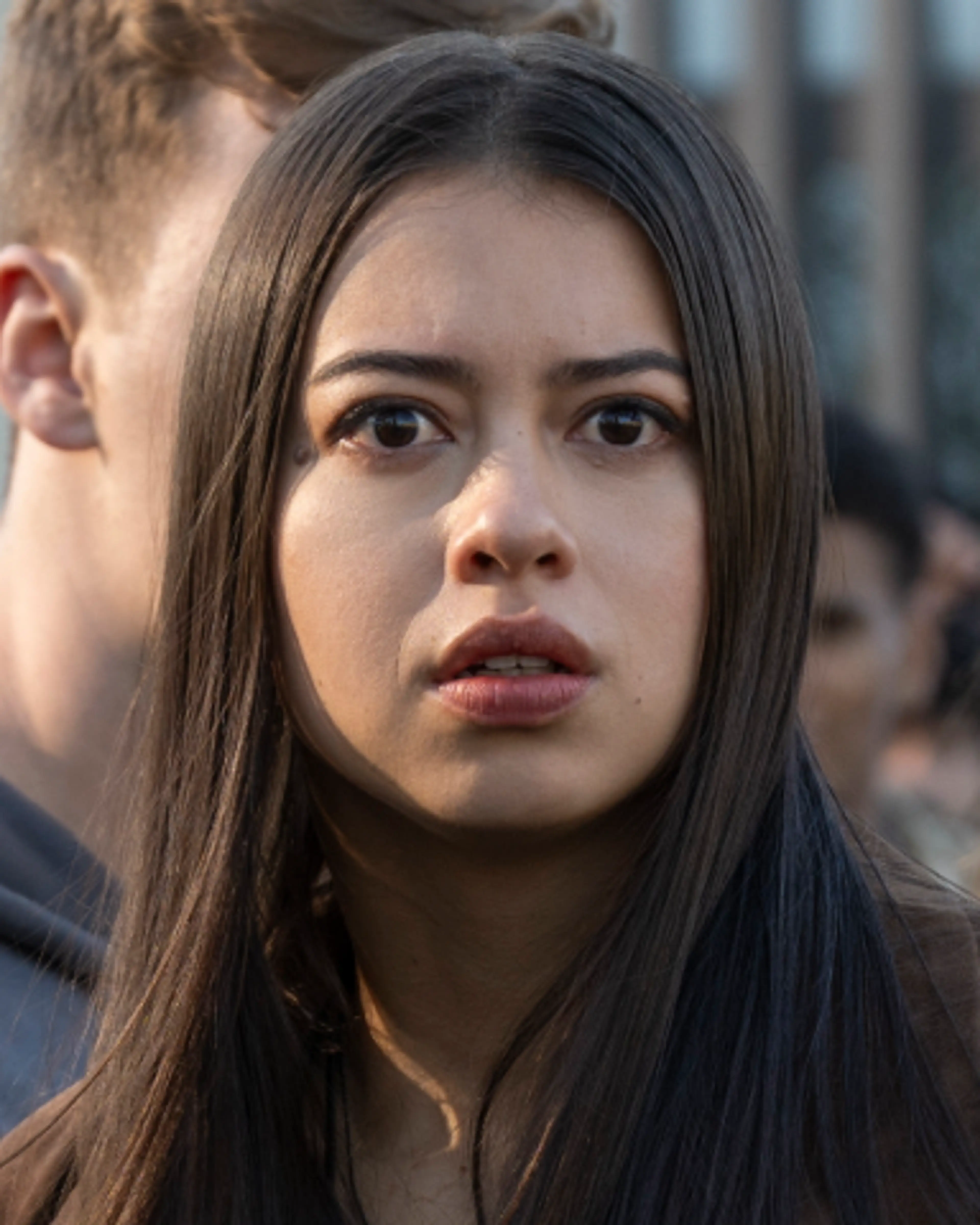 Amber Midthunder as Rita Desjardin stands among a crowd and looks toward someone in front of her.