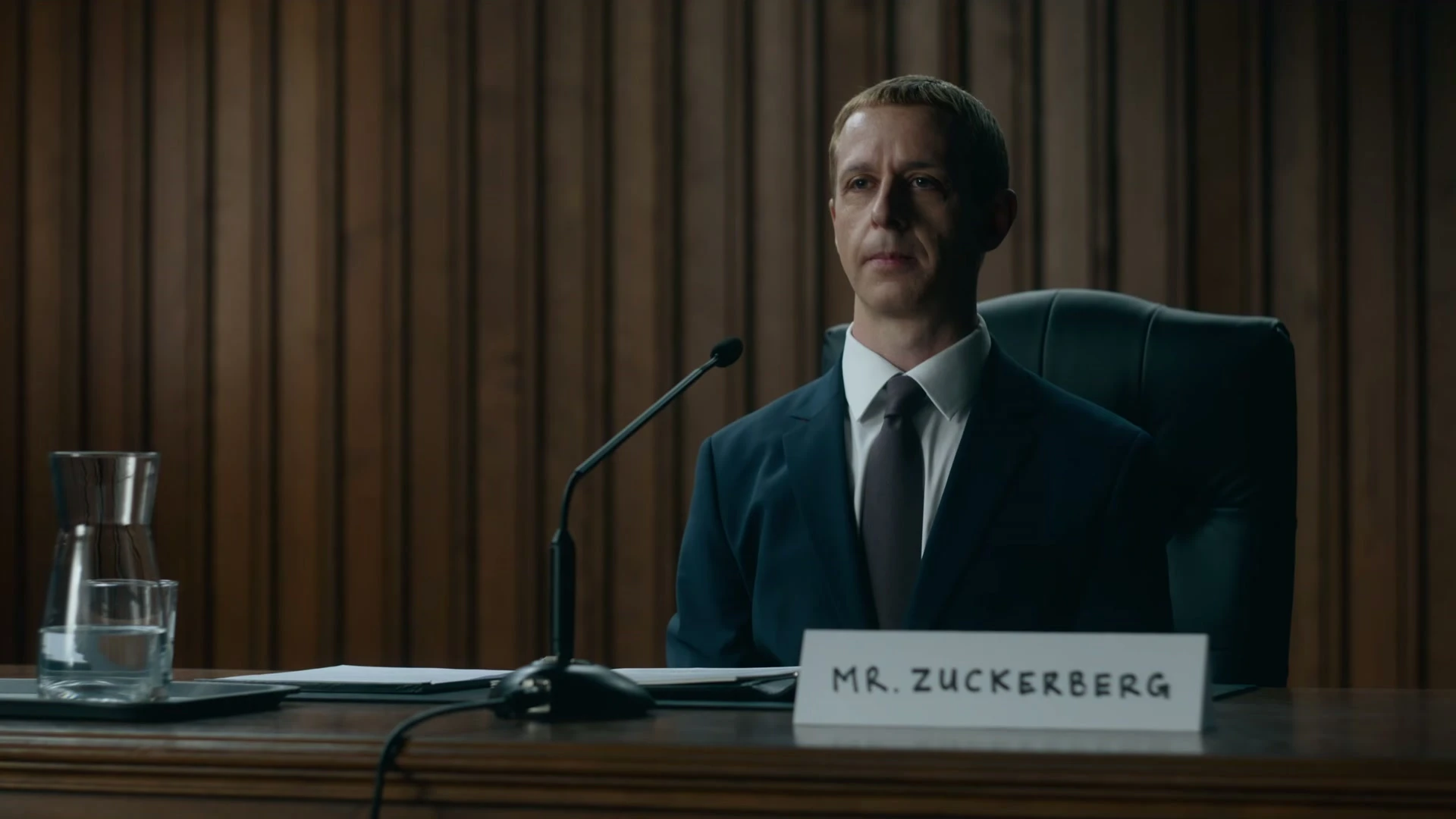 Jeremy Strong sits at a hearing table as Mark Zuckerberg in The Social Reckoning.