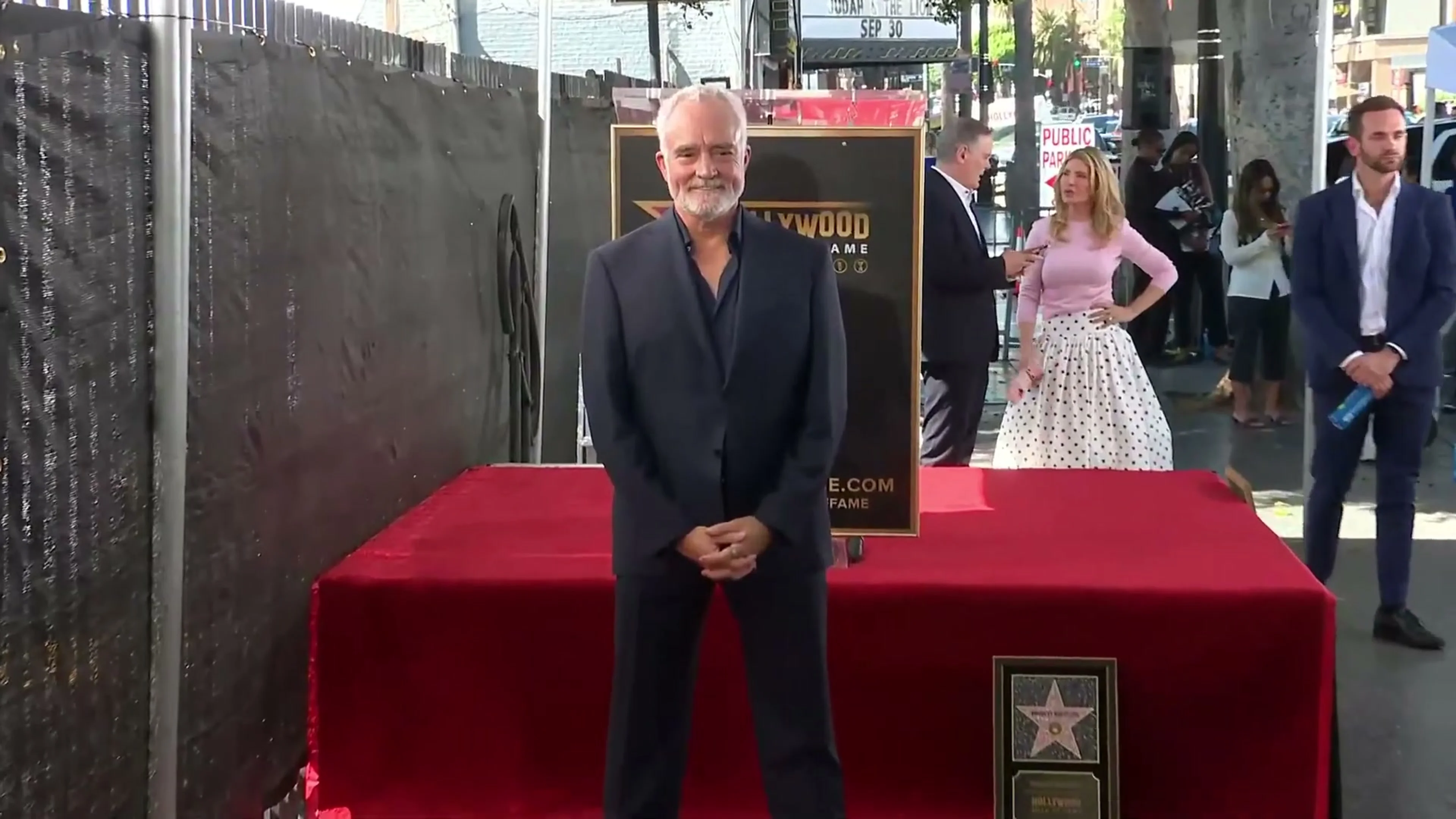 Bradley Whitford smiles in front of the Hollywood Walk of Fame display, with his framed plaque beside him.