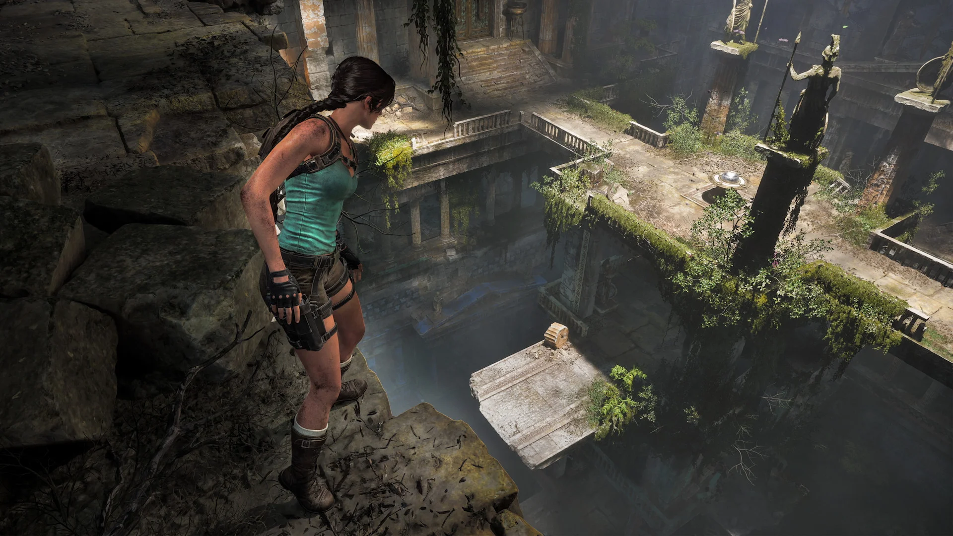 Lara Croft looks down into a deep Greek chamber with platforms, statues, and a movable stone block.