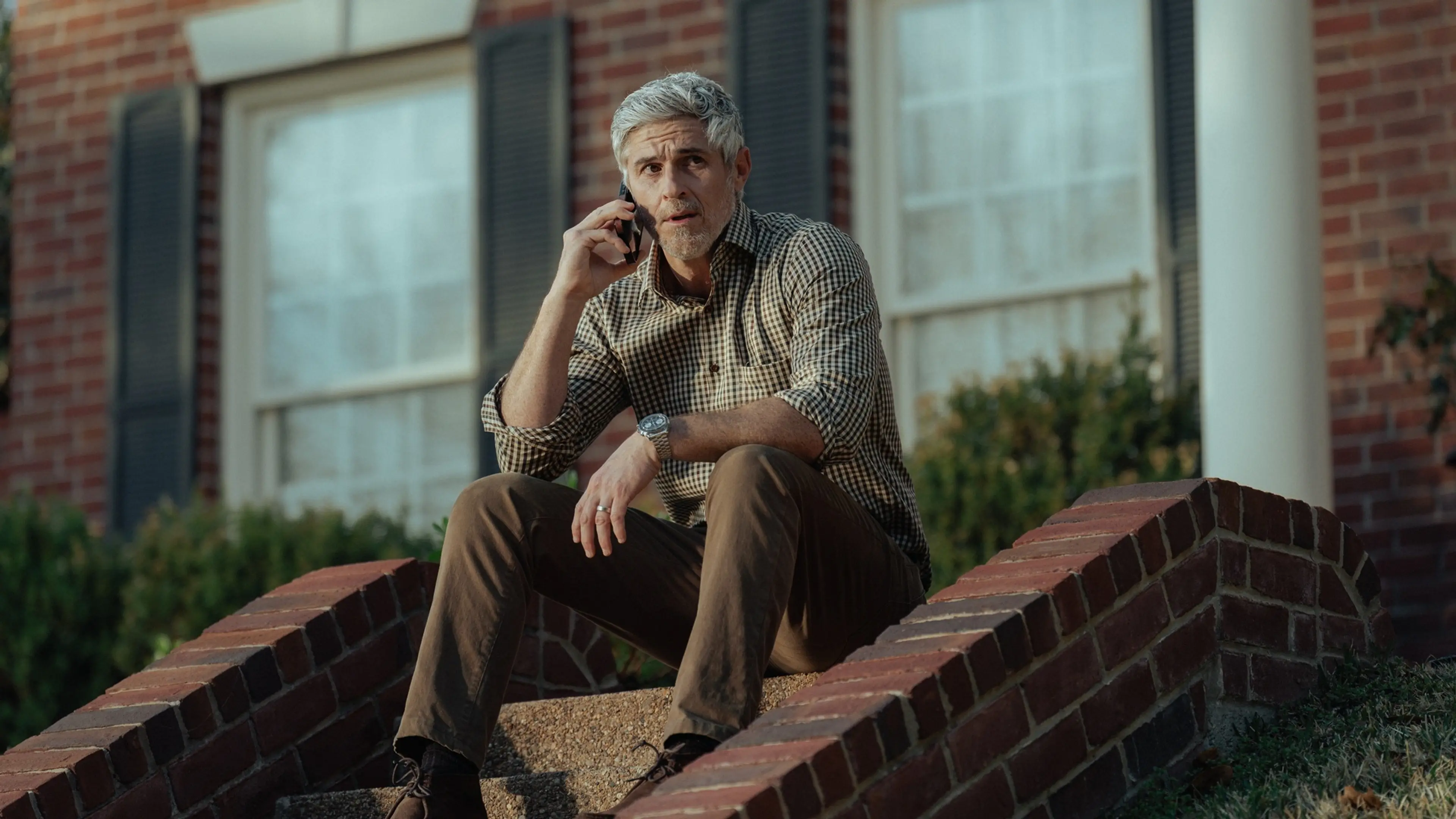 Dave Annable as Neal sits on outdoor steps while talking on a phone in Lioness Season 3.