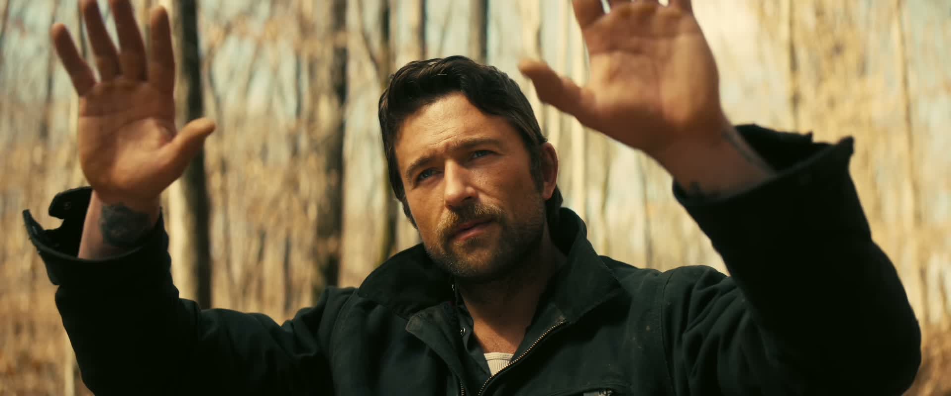 The cowboy raises his hands in the woods.