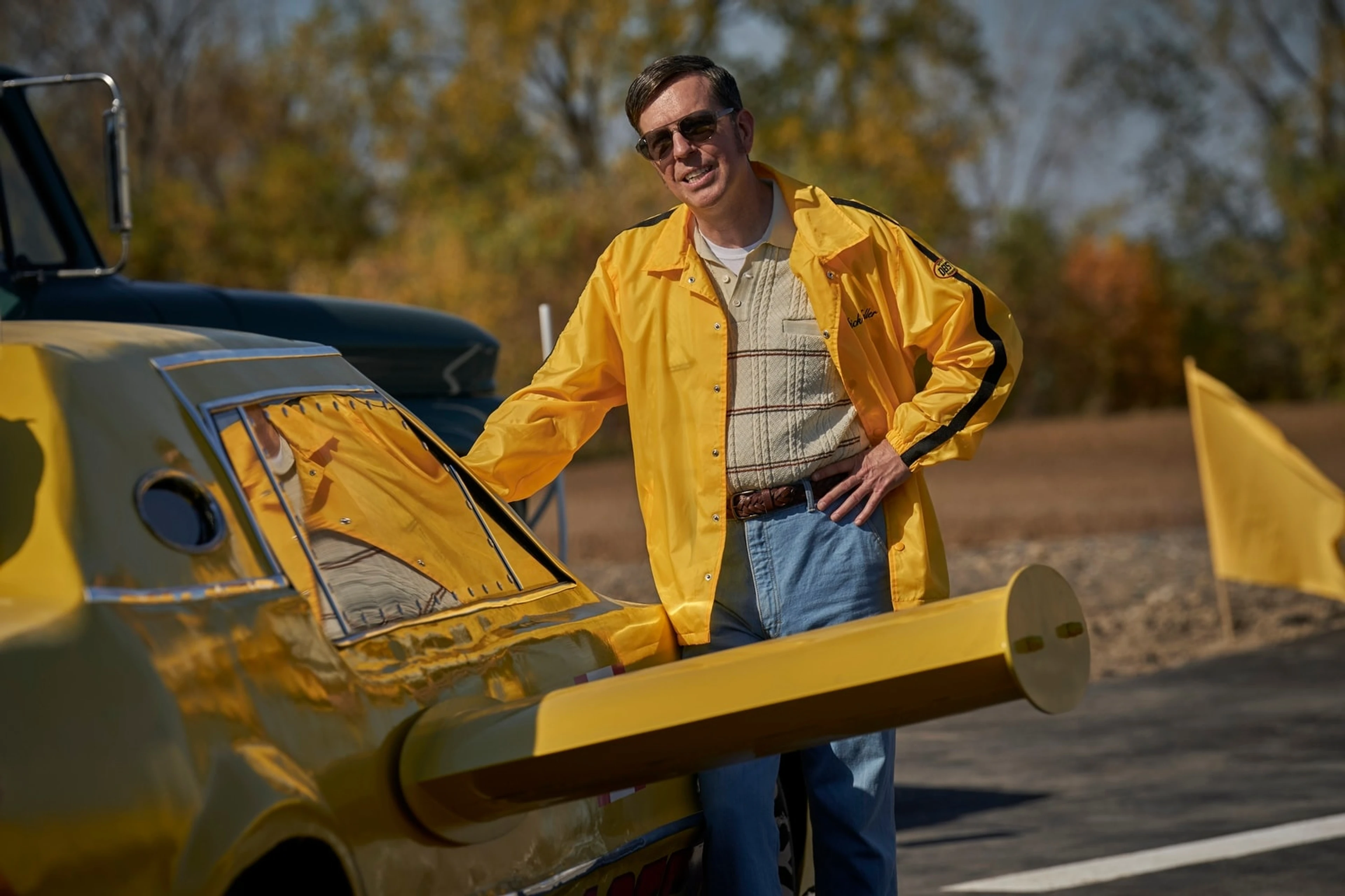 A man in a yellow jacket stands beside a yellow rocket car in The Stunt Driver.