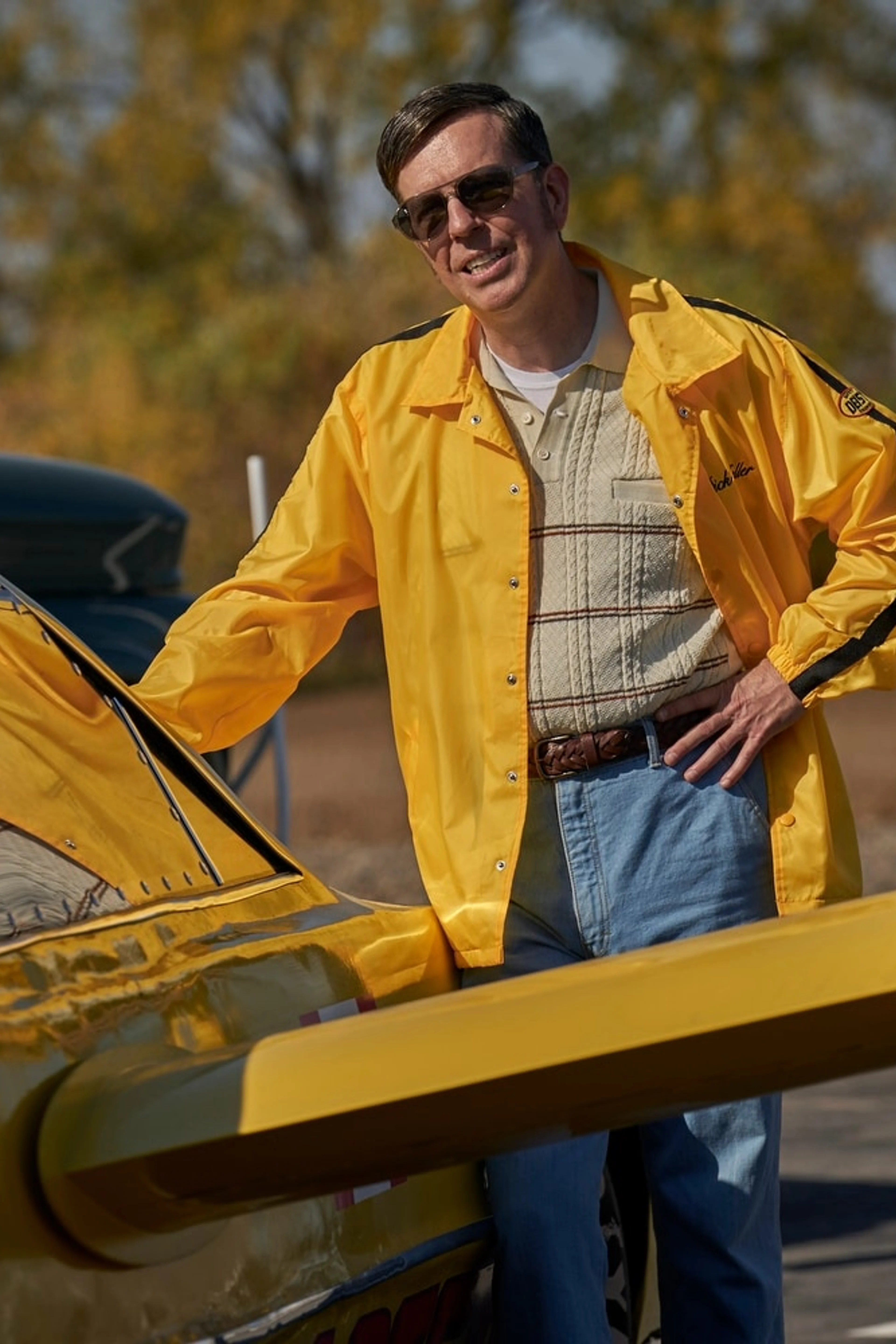 A man in a yellow jacket stands beside a yellow rocket car in The Stunt Driver.