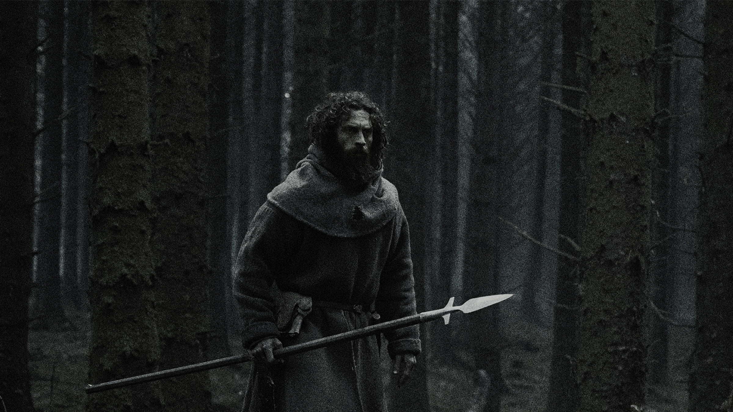 Aaron Taylor-Johnson stands in a dark forest holding a long spear in Werwulf.