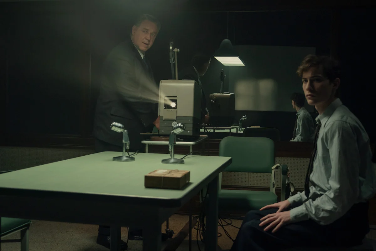 Henry Murray stands beside a projector while Ted Kaczynski sits at a table fitted with microphones.