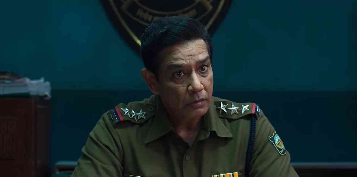Anup Soni as Inspector Khurana sits behind a desk in his police uniform.