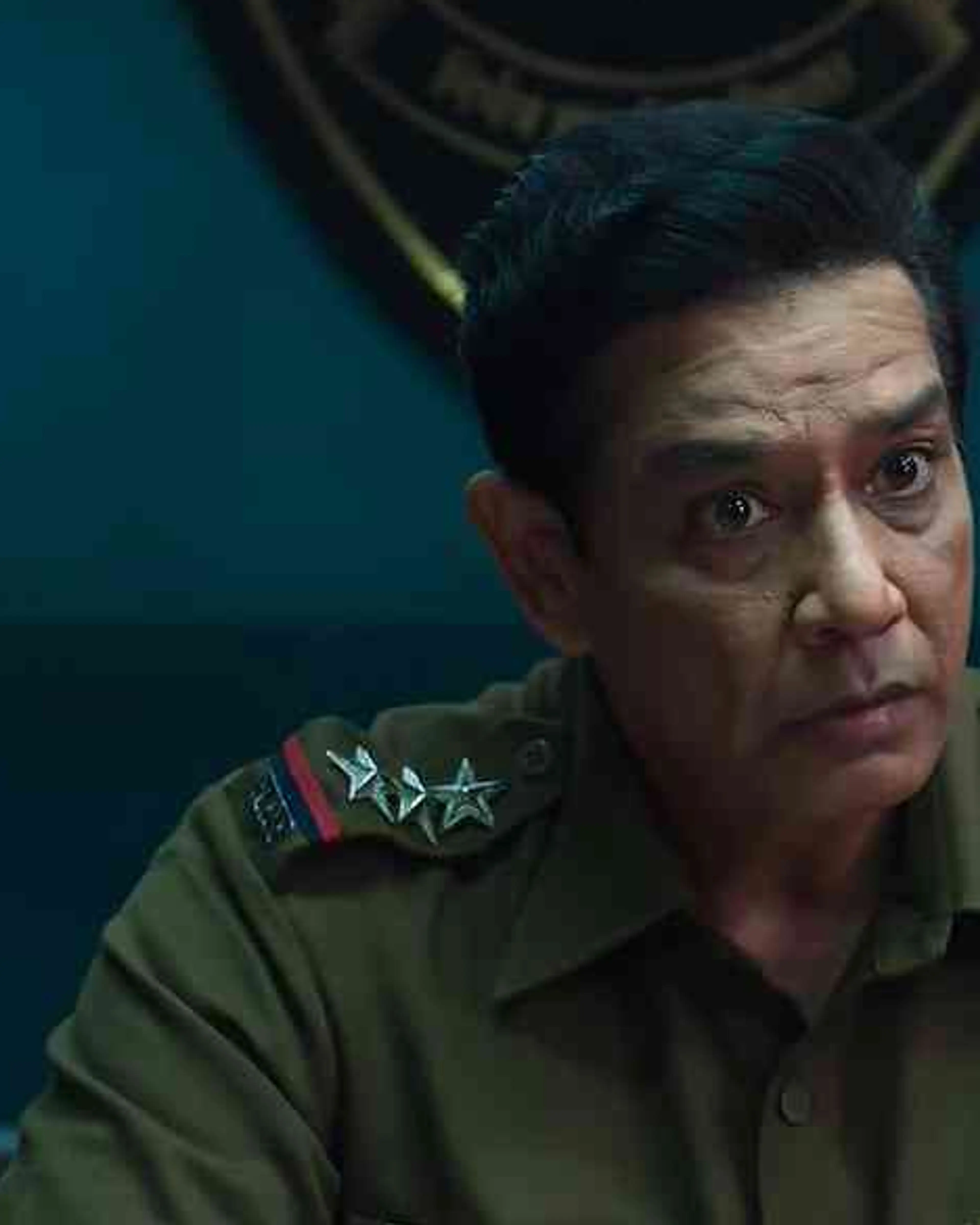 Anup Soni as Inspector Khurana sits behind a desk in his police uniform.