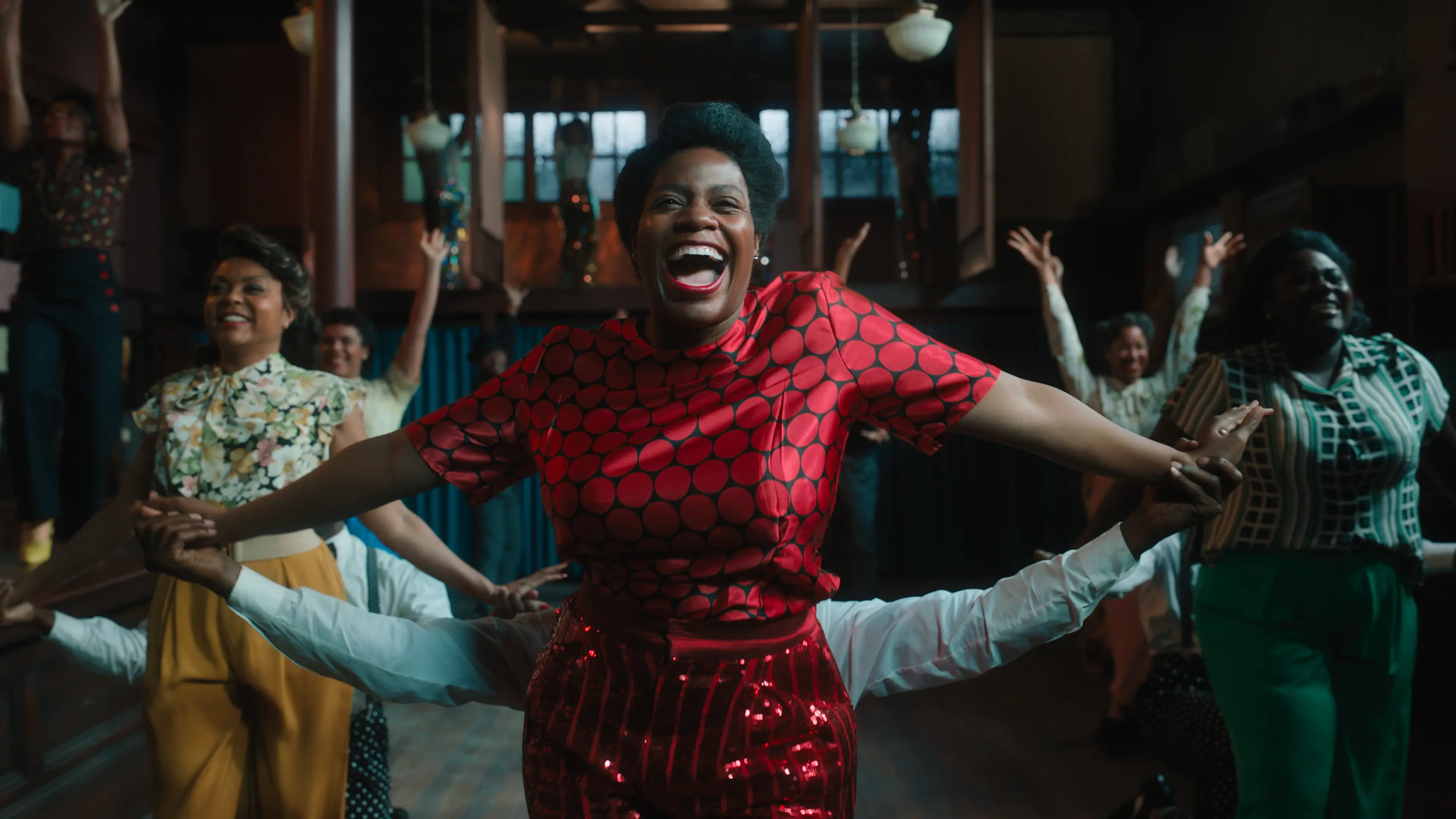 A musical ensemble performs indoors around a singer in a red patterned outfit in The Color Purple (2023).