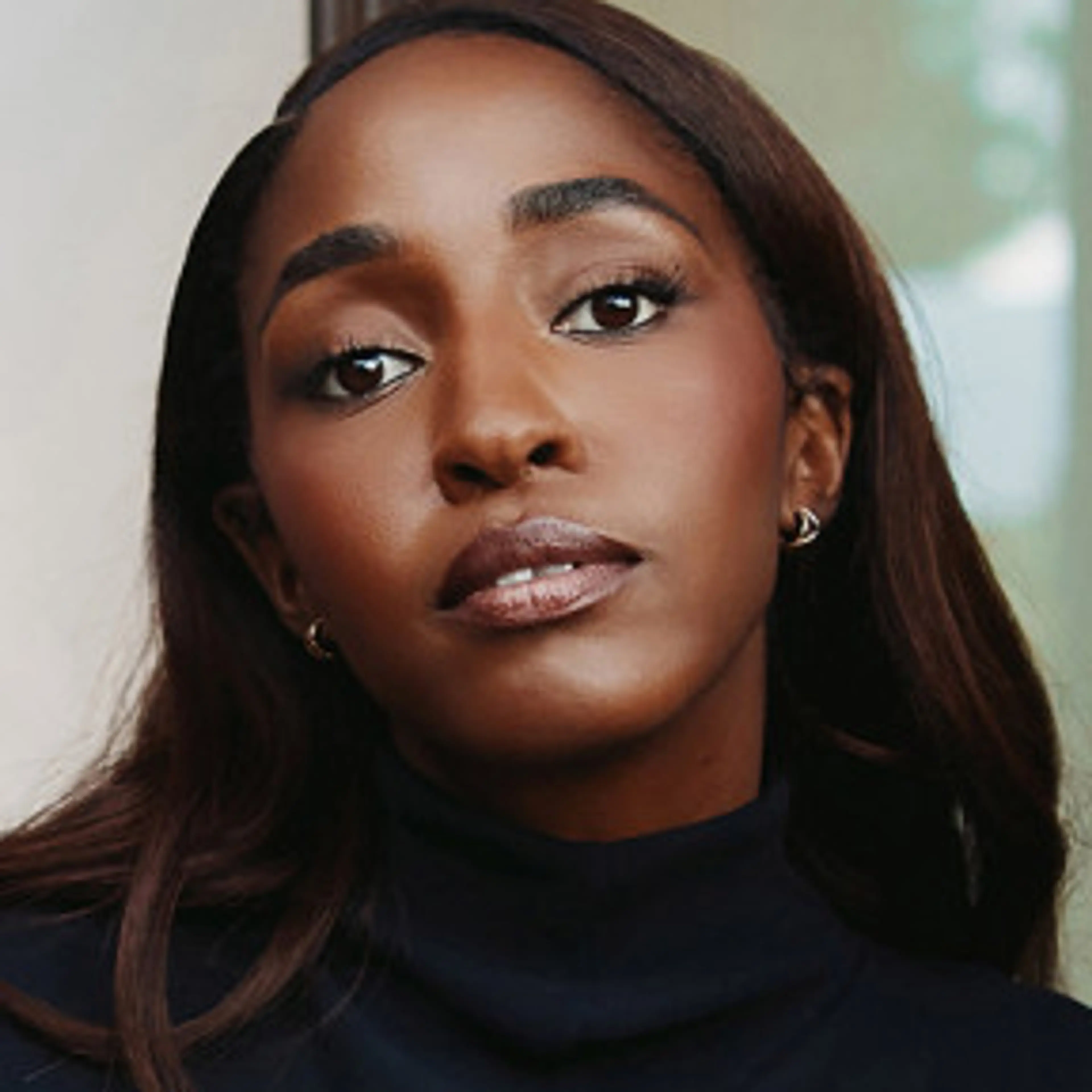 Ayo Edebiri wears a dark high-neck top with her hair falling over her shoulders.