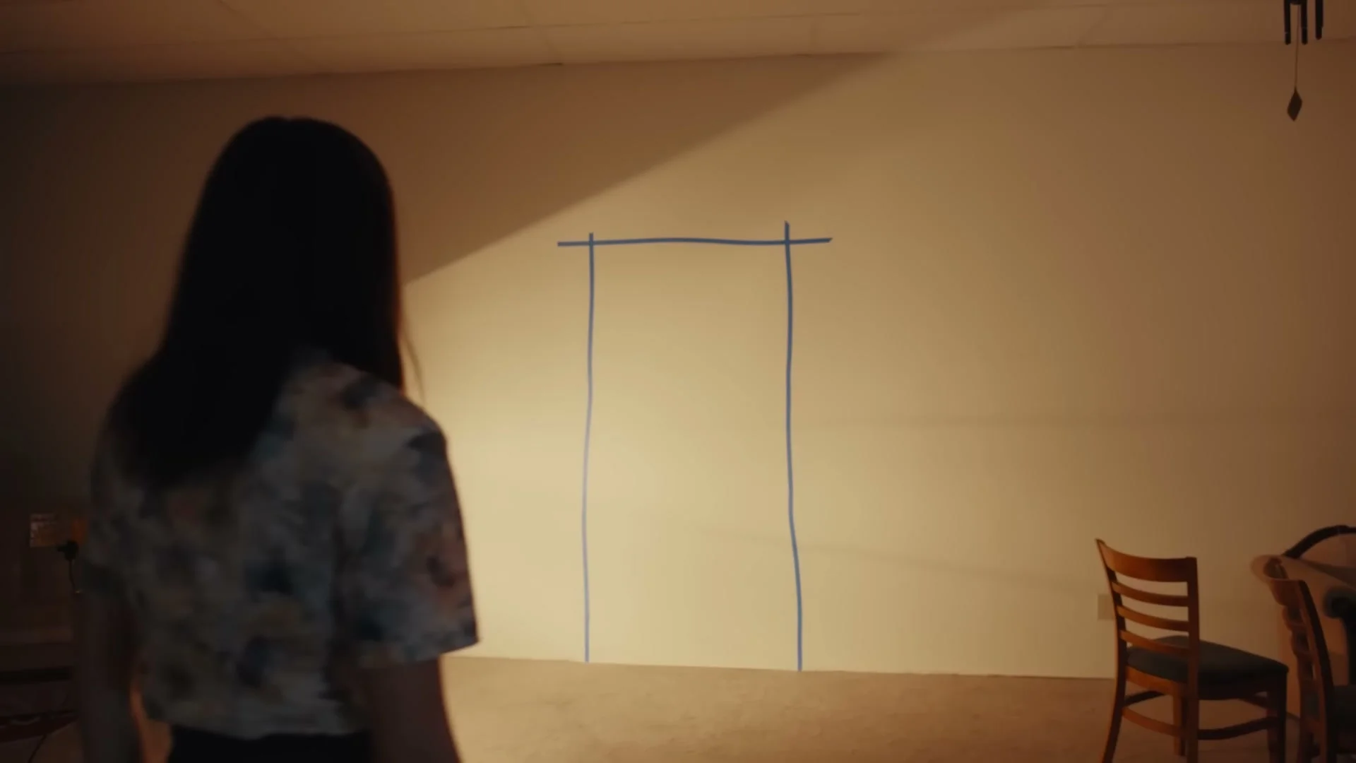 Mary faces a doorway outlined in blue tape between furniture displays.