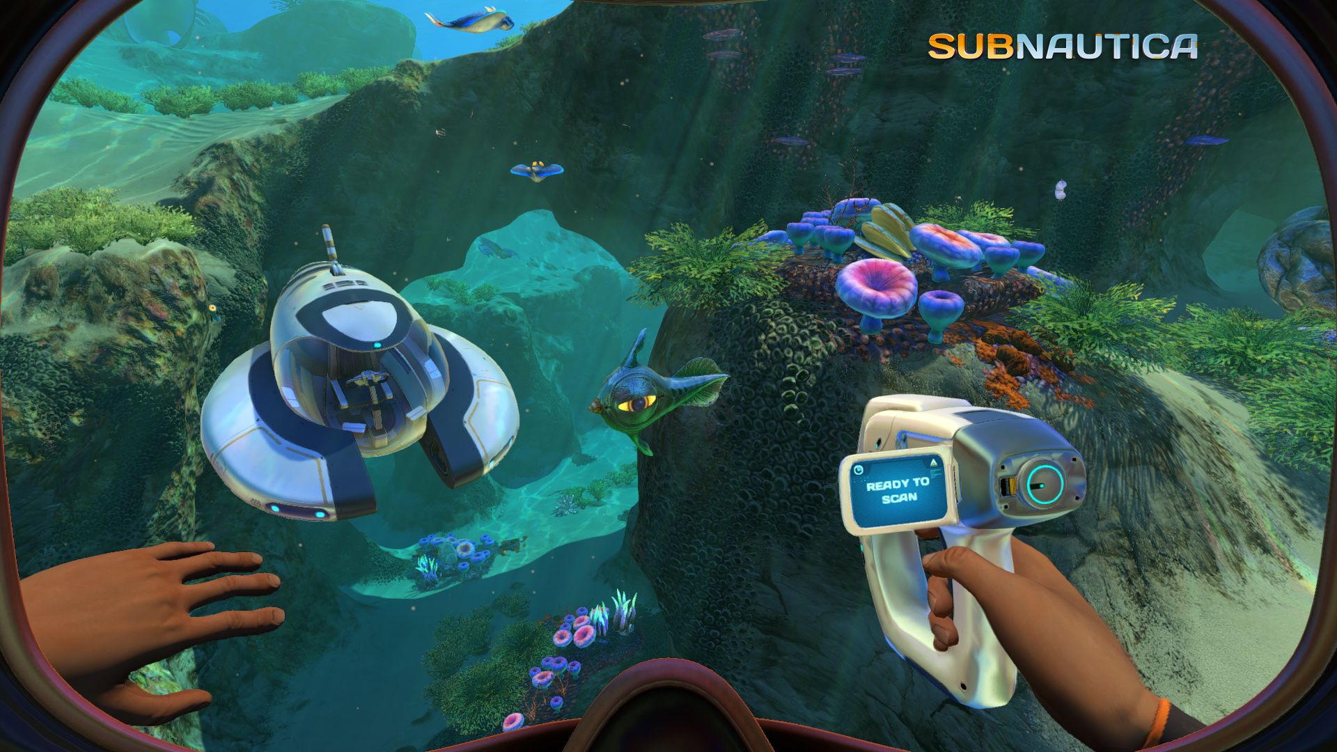 A Subnautica diver holds a handheld tool near a small underwater vehicle and colourful reef.