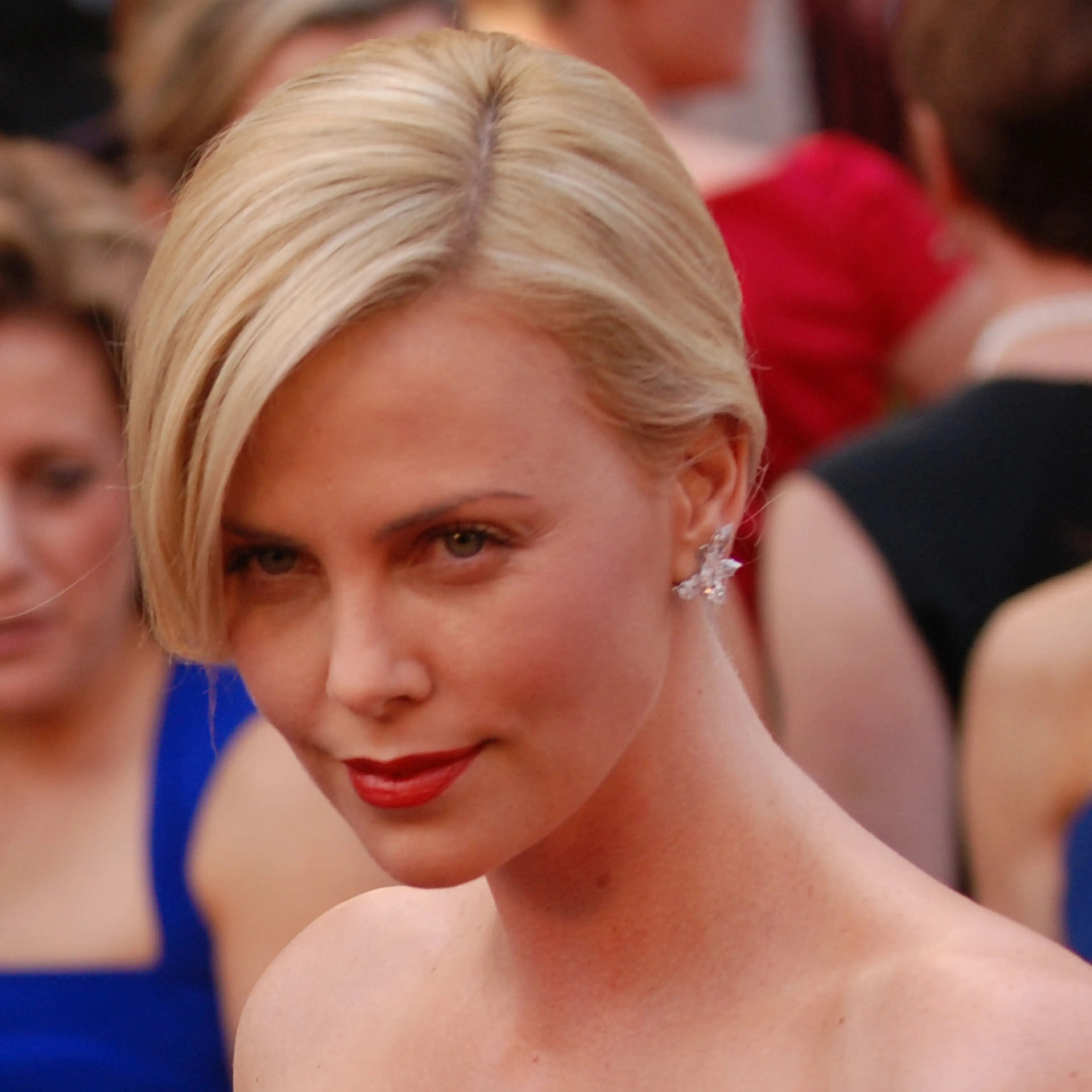 Charlize Theron at the 2010 Academy Awards, with blonde hair and red lipstick.