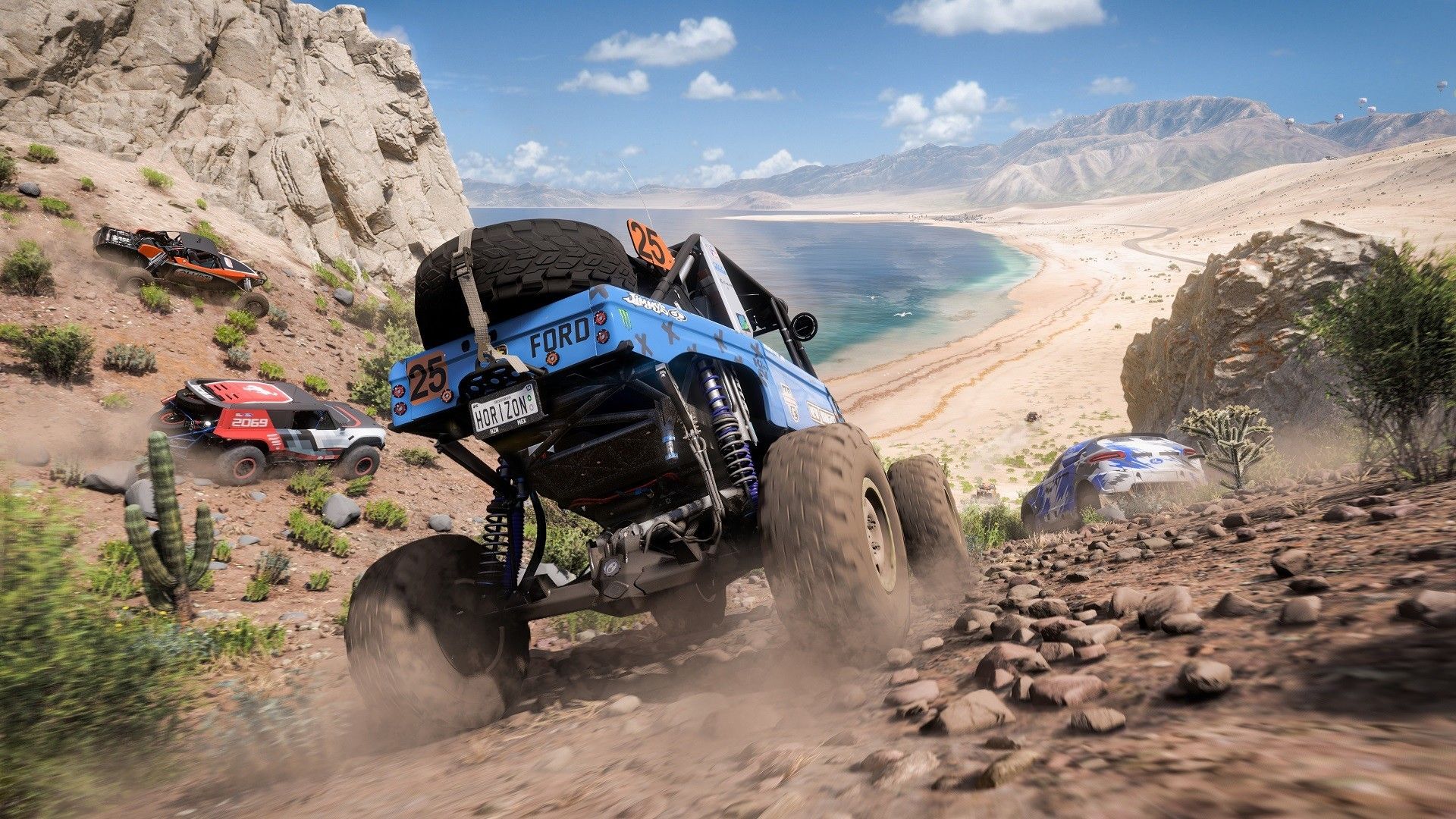 Off-road trucks descend a rocky hill toward a beach.