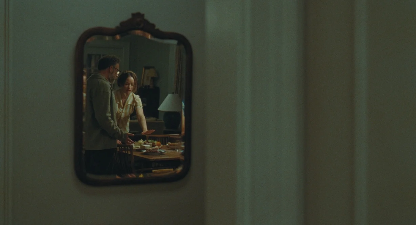 Joe and Angela appear in a small mirror on an otherwise empty wall.