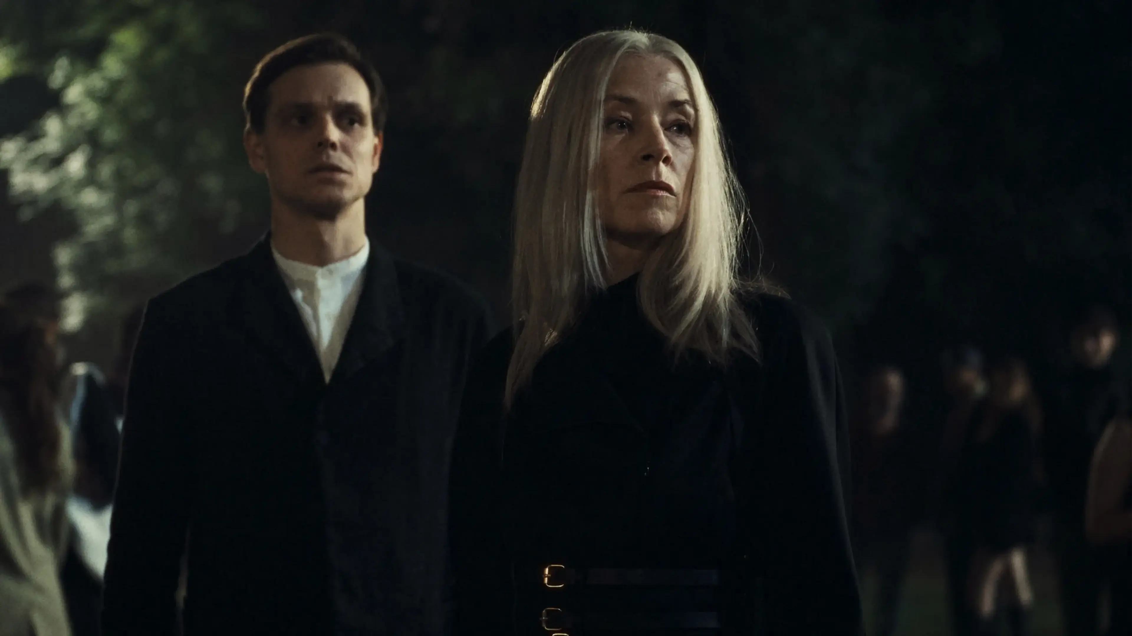 Two figures dressed in black stand at a nighttime gathering in City of Blood.
