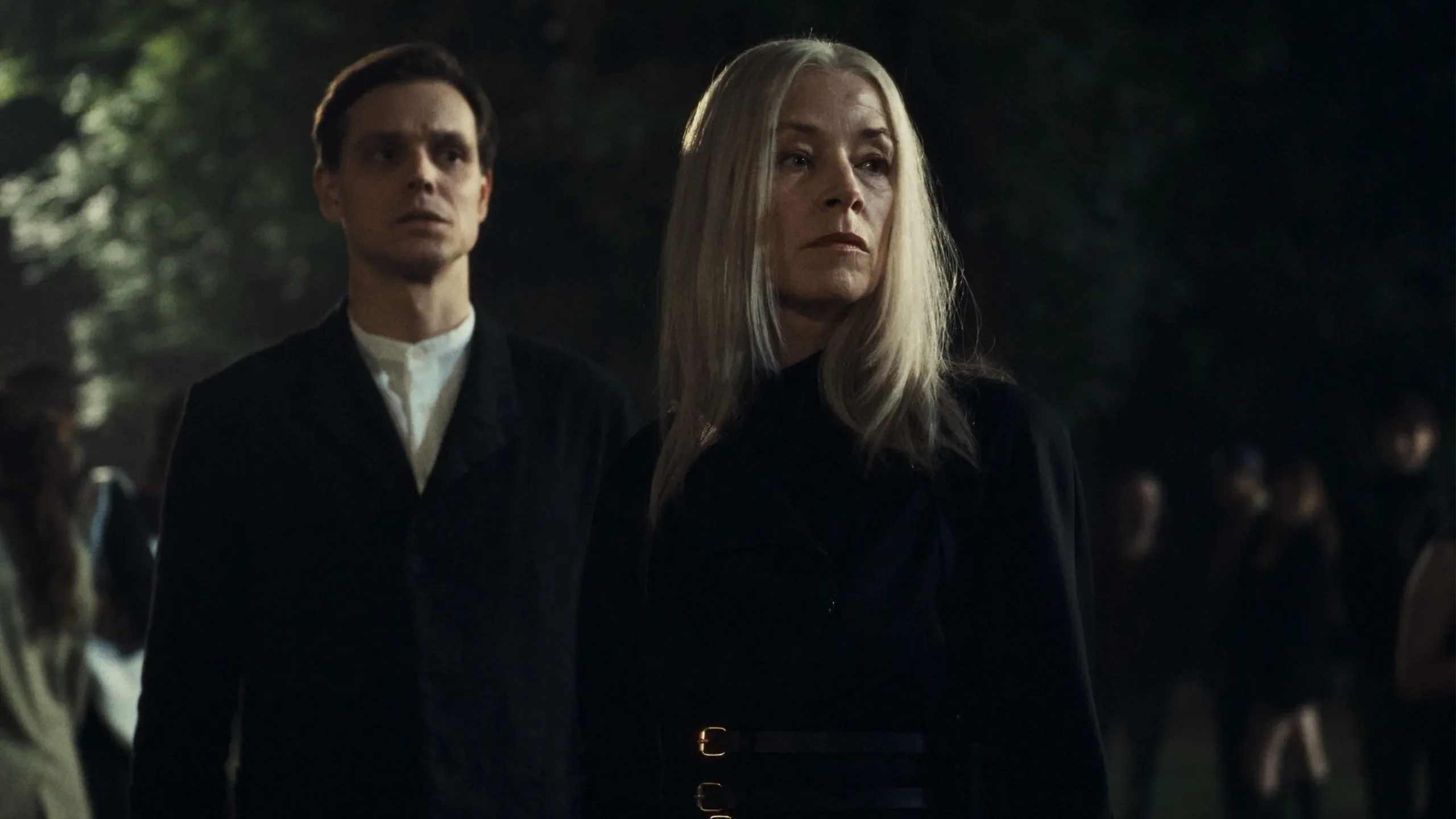 Two figures dressed in black stand at a nighttime gathering in City of Blood.