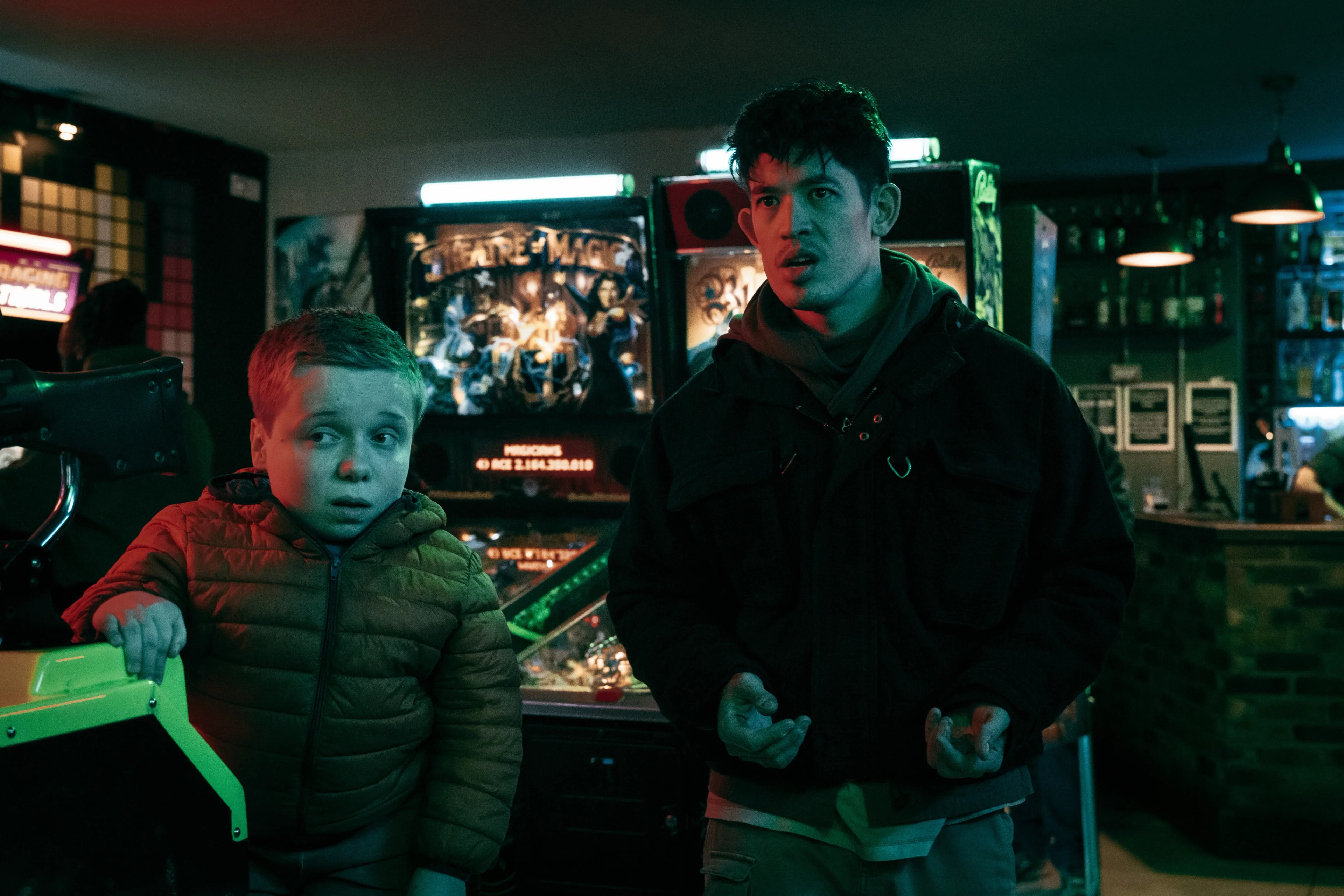 Reece Nesmith and Roddy Ho stand beside arcade machines under colored lights.