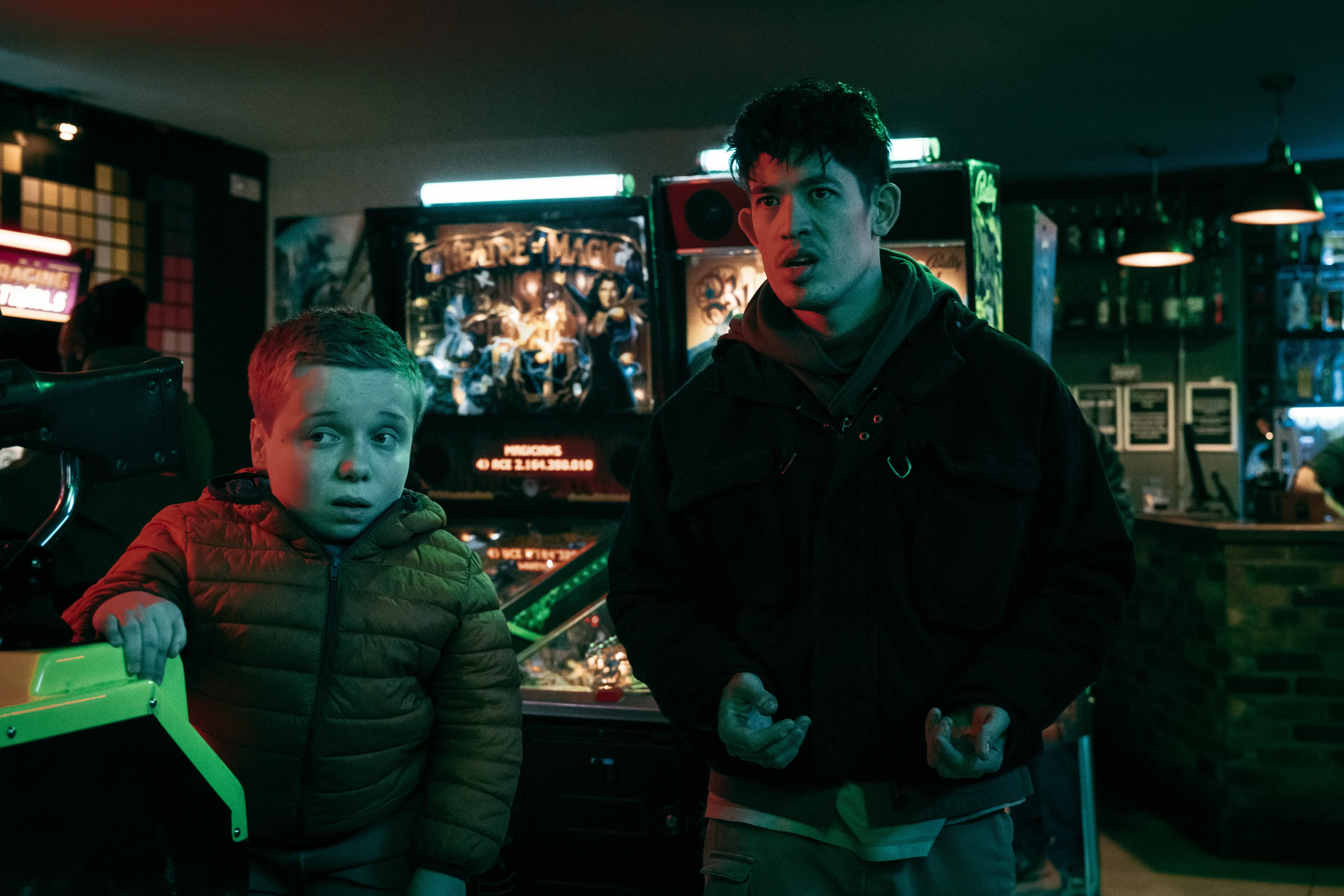 Reece Nesmith and Roddy Ho stand beside arcade machines under colored lights.