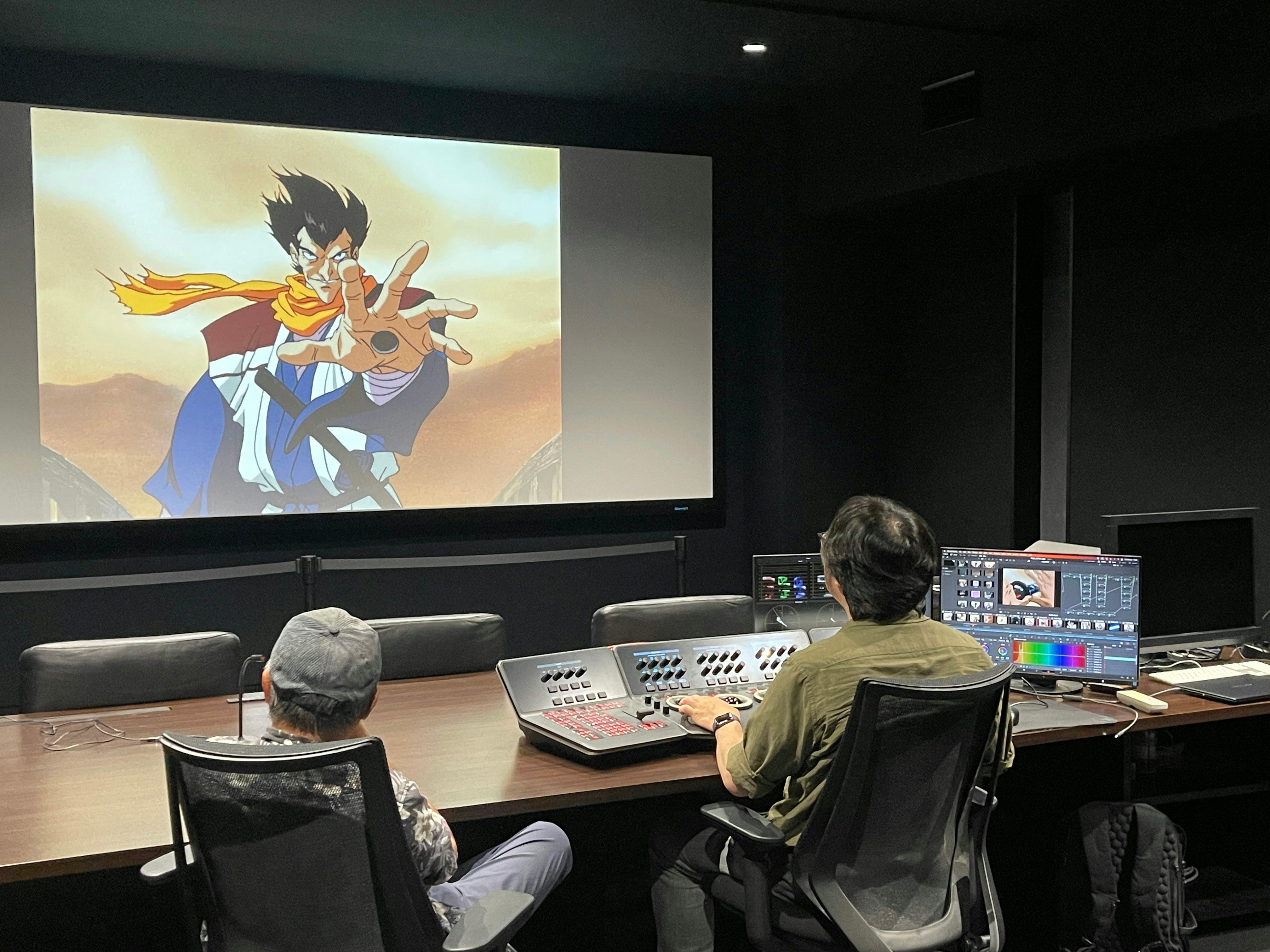 The restoration team reviews an animated character on a large screen beside monitors and color controls.